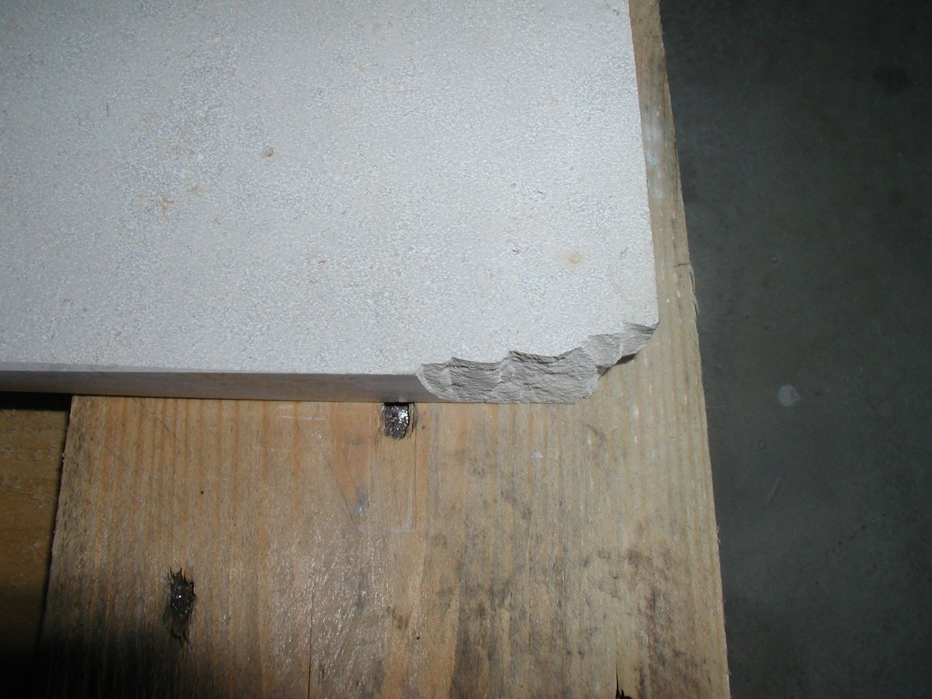 Beschädigte Ecke einer hellen Fliese, die auf einer Holzoberfläche liegt.