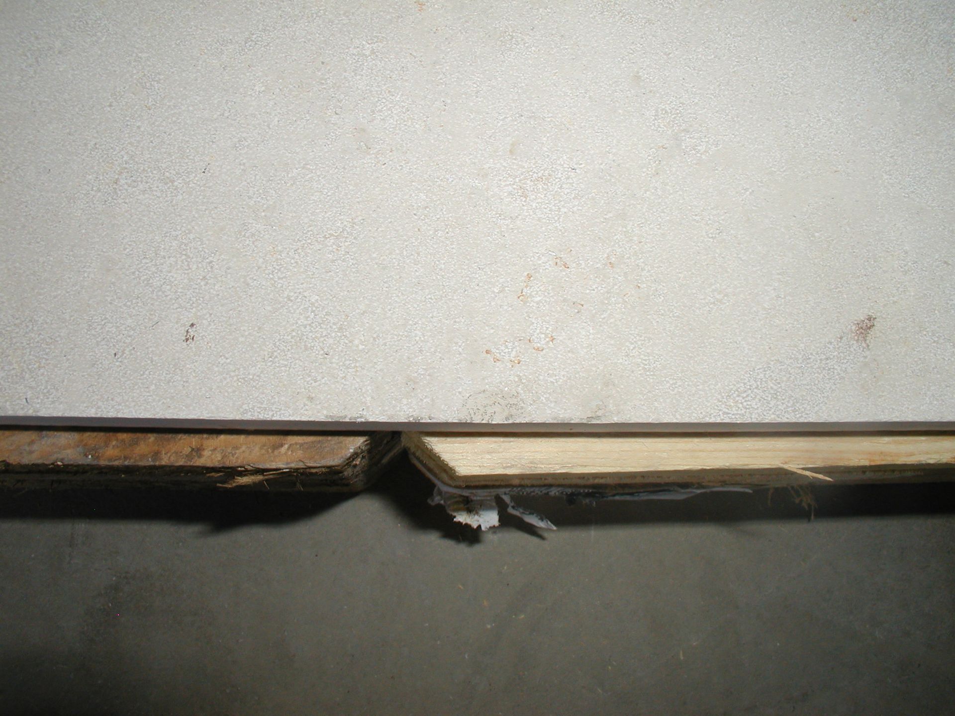 Beschädigte Dielen und Wände, mit einer Lücke dazwischen. Hellbraunes Holz und weiße Wand.