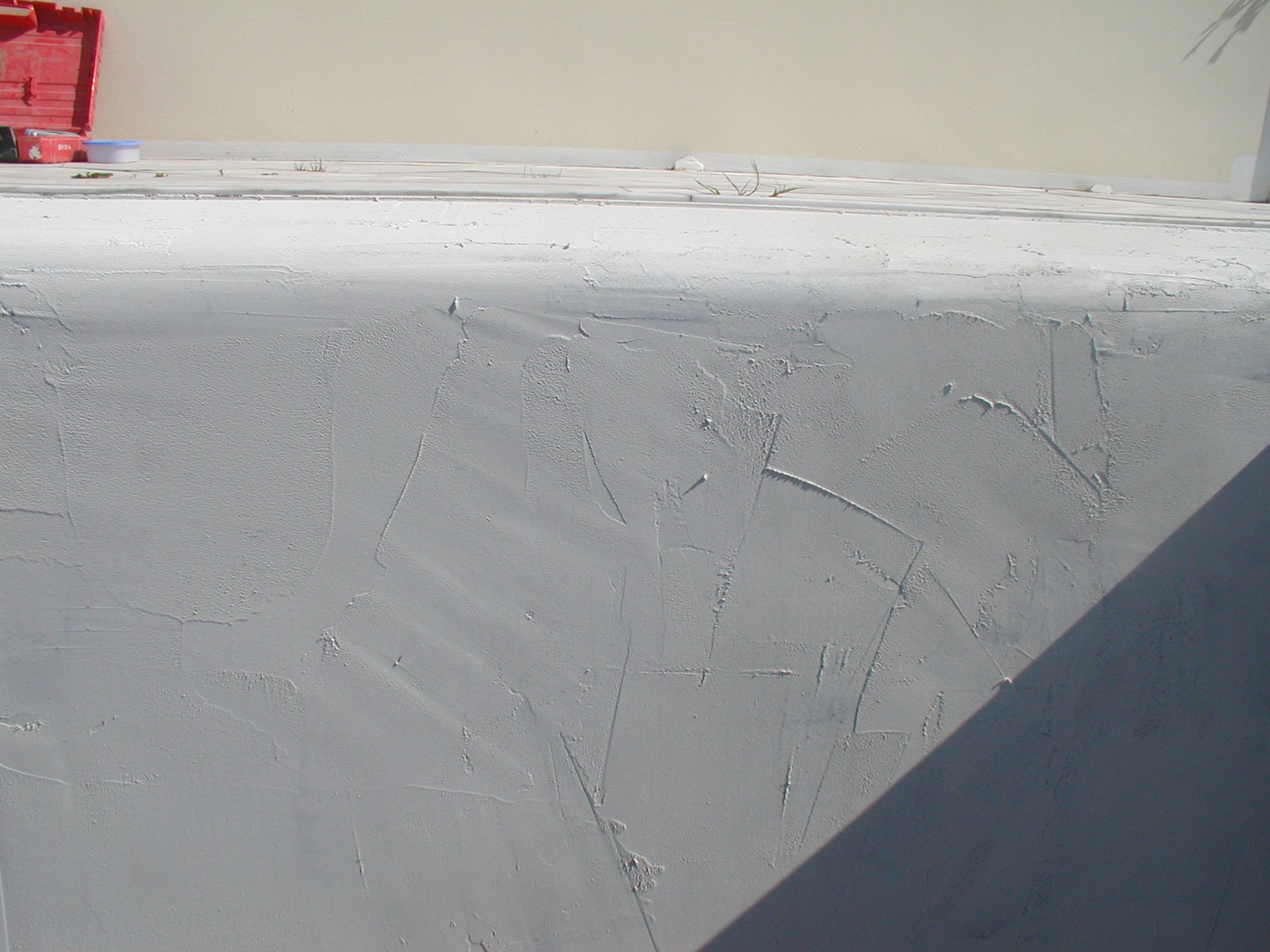 Graue Stuckwand mit strukturierter Oberfläche, Sonnenlicht wirft Schatten.