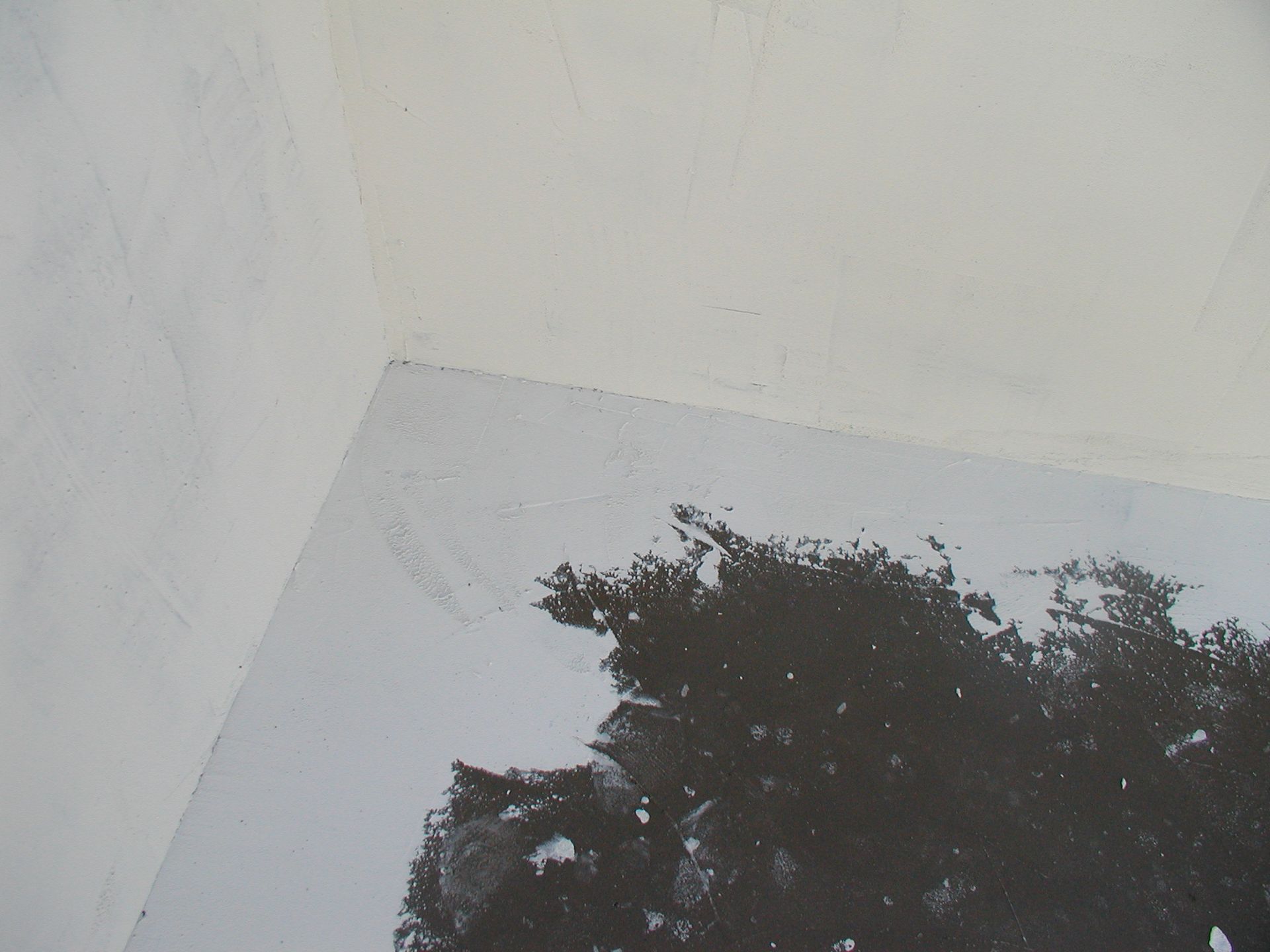 Zimmerecke, weiße Wände und Decke, dunkle Flecken auf dem Boden.