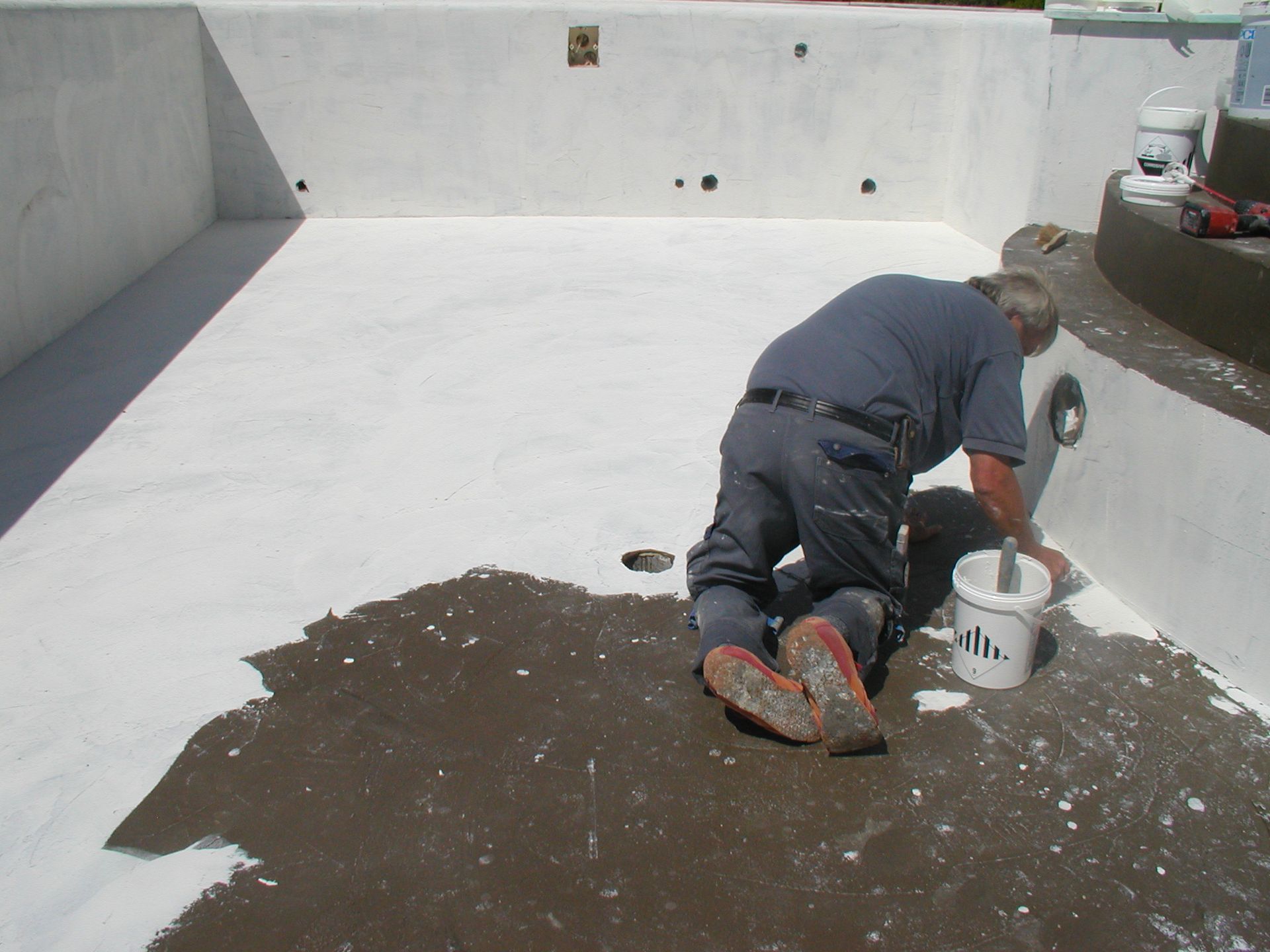 Person, die den Boden eines leeren Schwimmbeckens mit weißer Farbe bemalt.