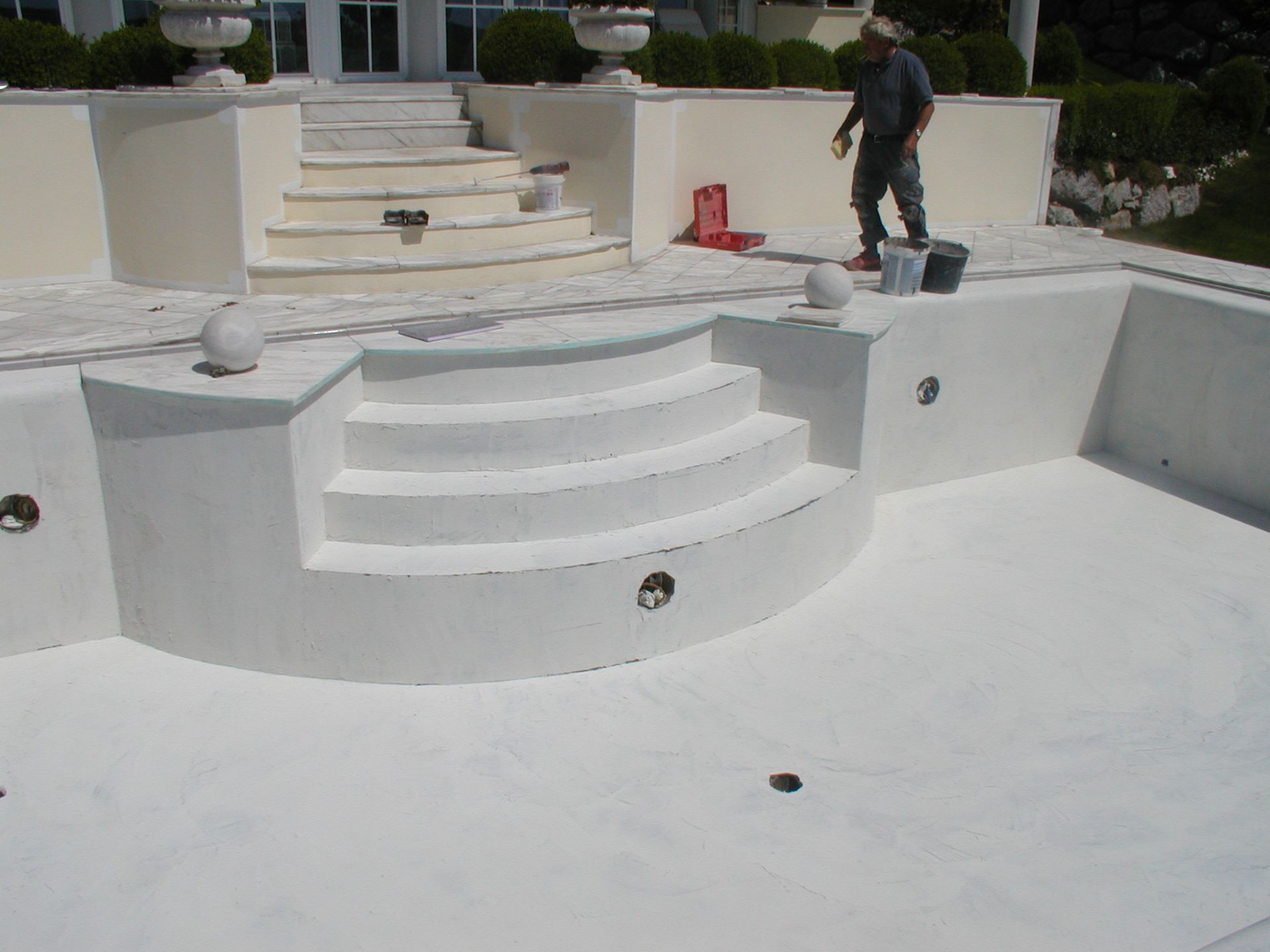 Weiß gestrichener Swimmingpool mit geschwungenen Stufen; ein Arbeiter steht in der Nähe.