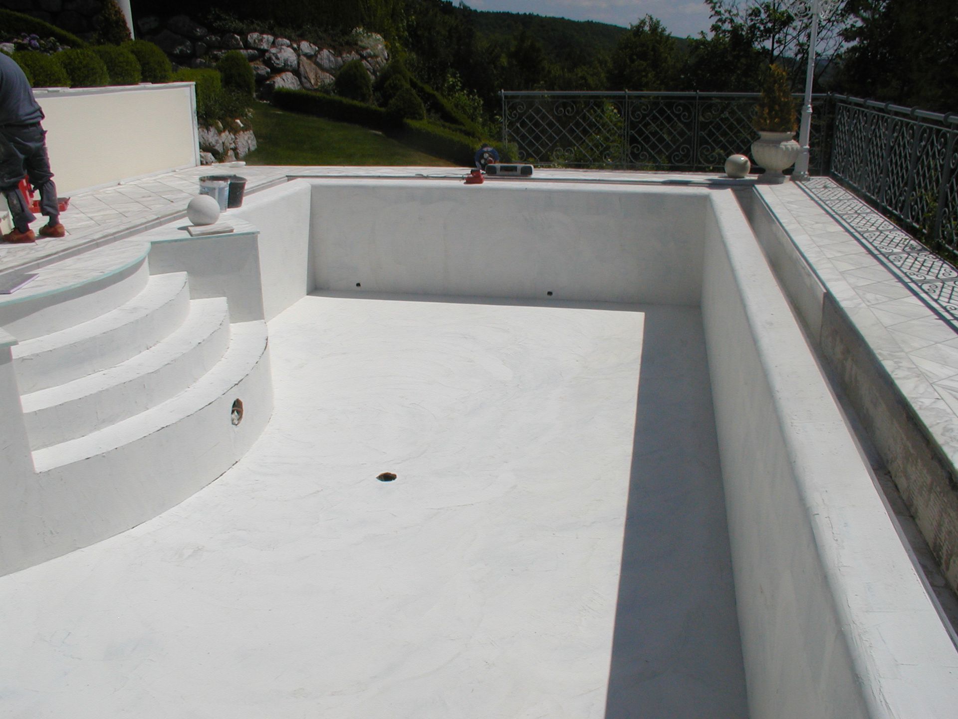 Leerer weißer Swimmingpool mit Stufen, umgeben von einem Betondeck.