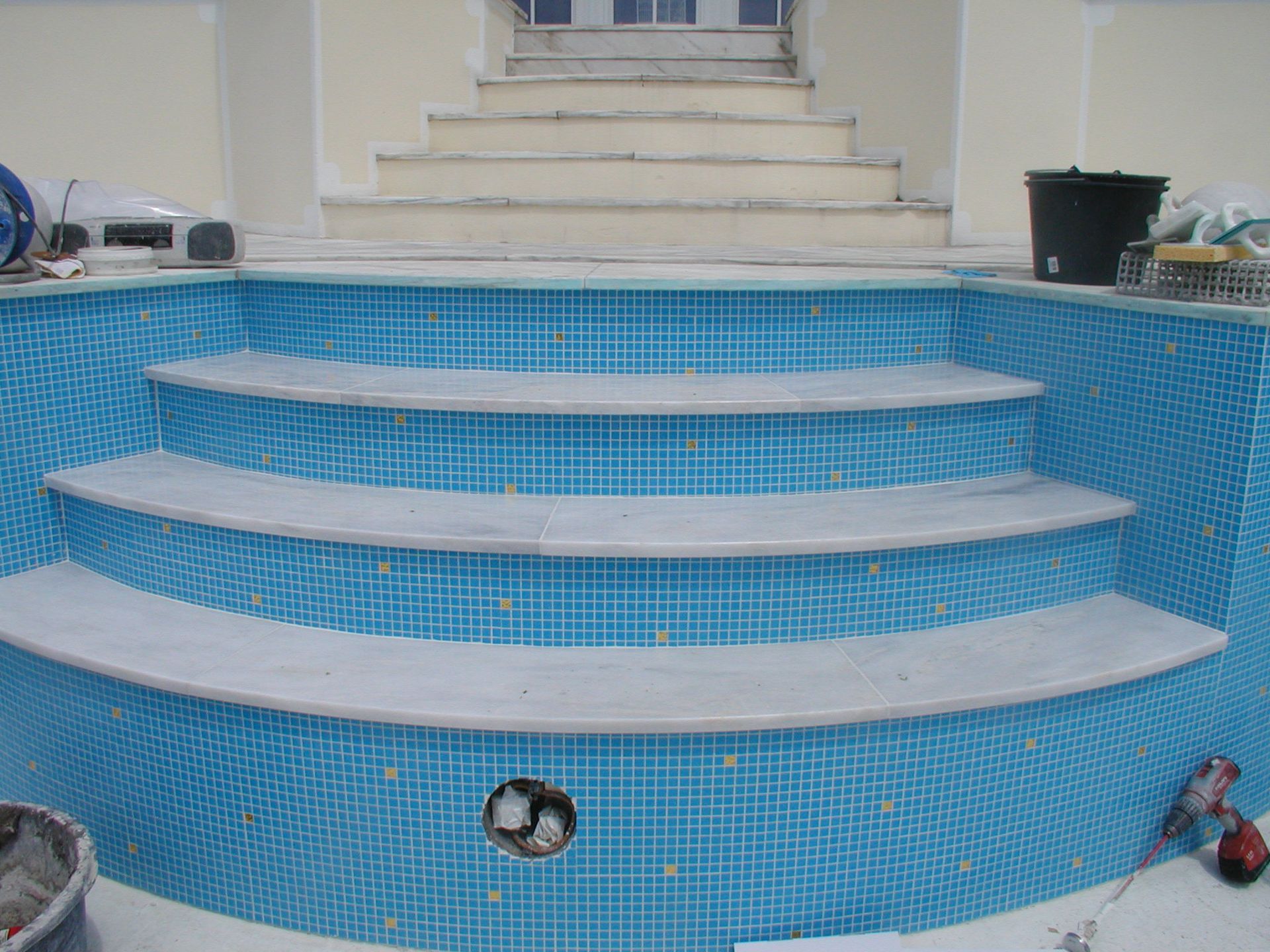 Blau geflieste Pooltreppe mit Marmorstufen, die zu einer Treppe führen.