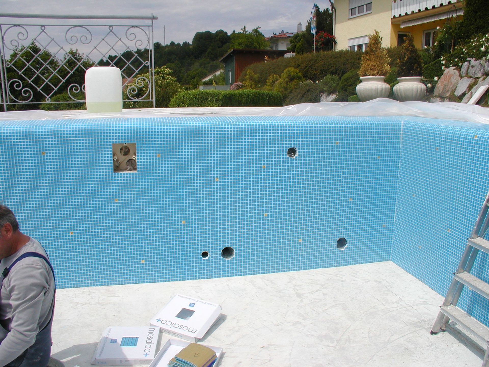 Ein Arbeiter verlegt blaue Mosaikfliesen in einem leeren Schwimmbecken.