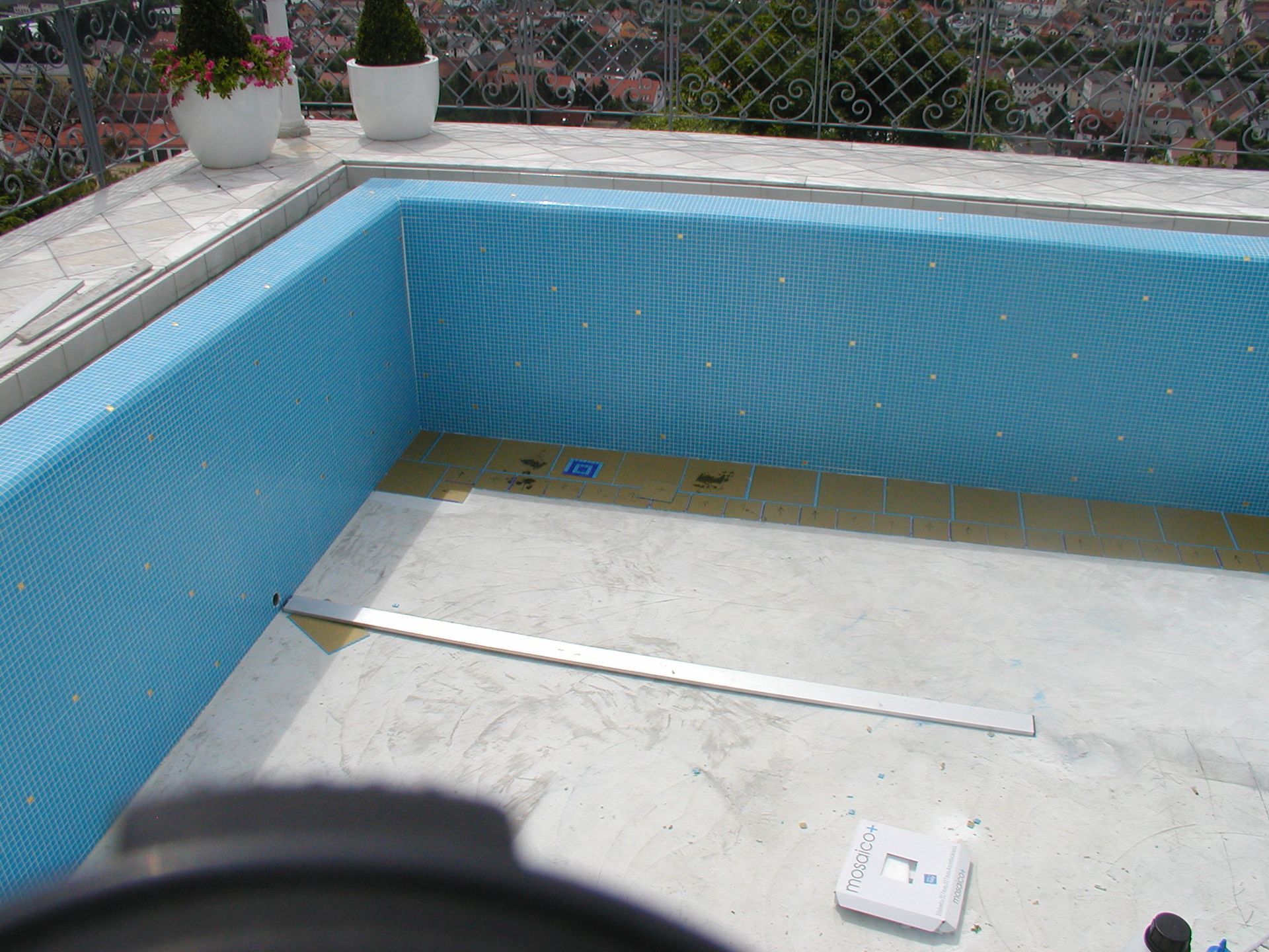 Im Bau befindlicher Pool mit blau gefliesten Wänden, Betonboden und Metallverkleidung.