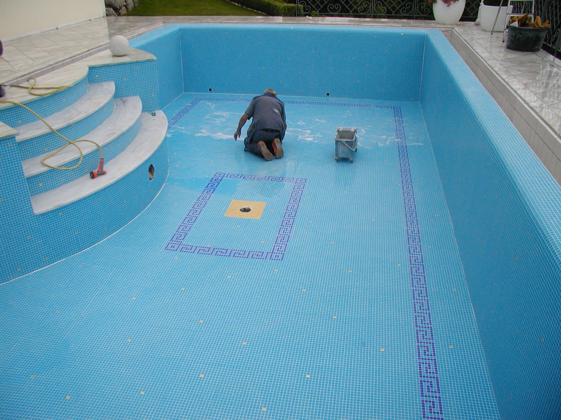 Person, die das Innere eines blau gefliesten Schwimmbeckens mit Treppe fliest; Umgebung im Freien.