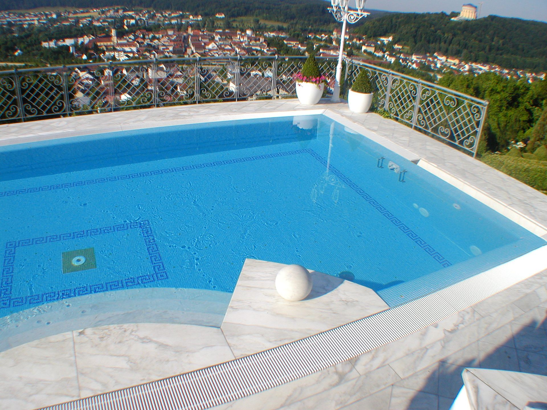 Ein Pool mit Marmorumrandung bietet Blick auf die Stadt. Blaues Wasser, weiße Akzente und ein sonniger Tag.
