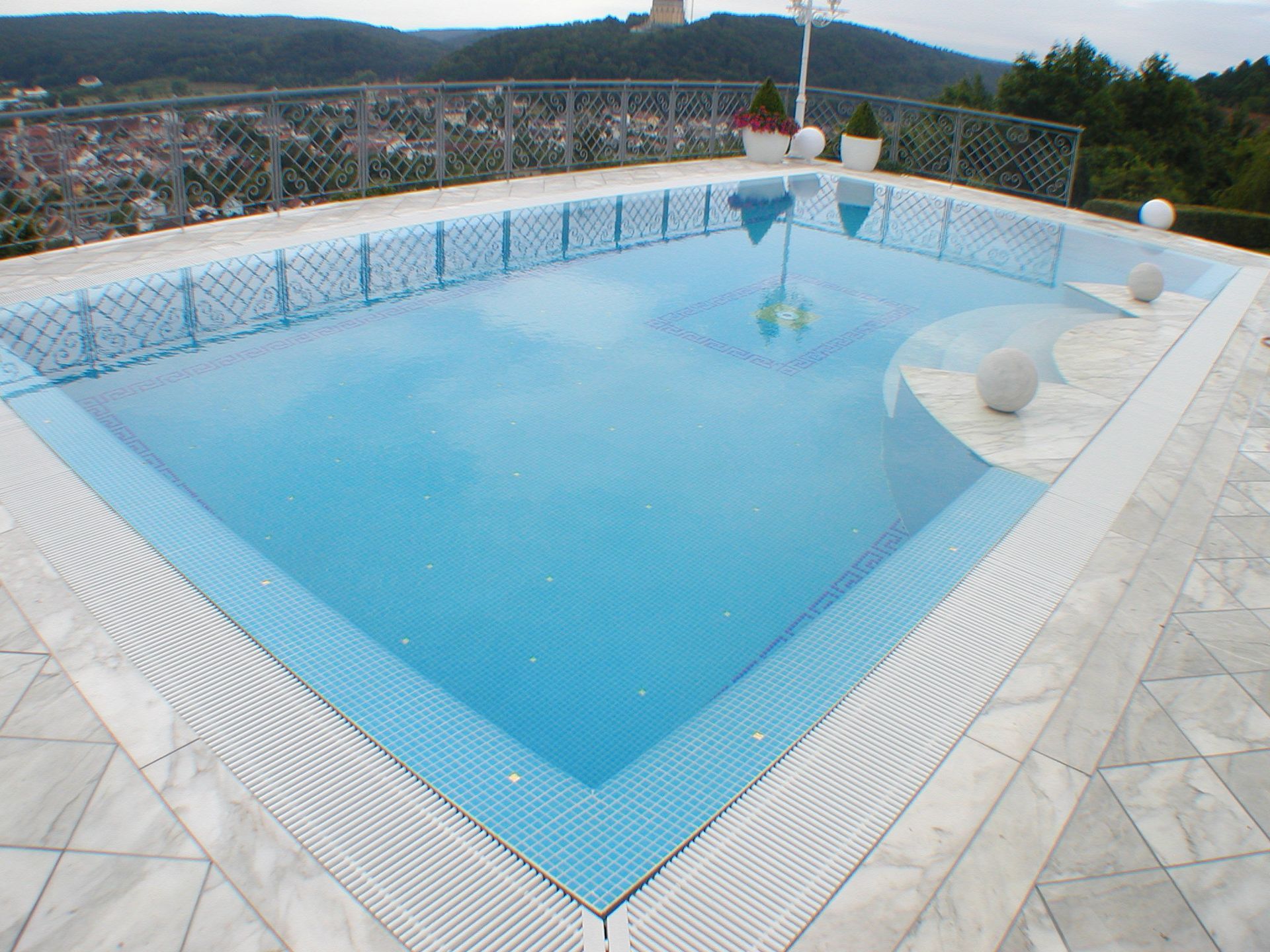 Ein Swimmingpool mit blauen Fliesen und weißen Verzierungen mit Blick auf eine Stadt.
