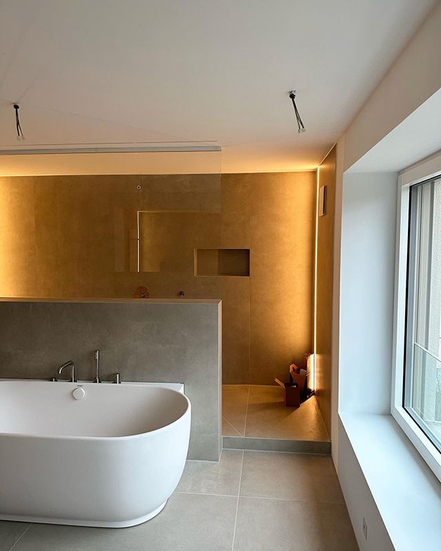 Modernes Badezimmer mit weißer Badewanne, neutralen Fliesen und warmer Beleuchtung.