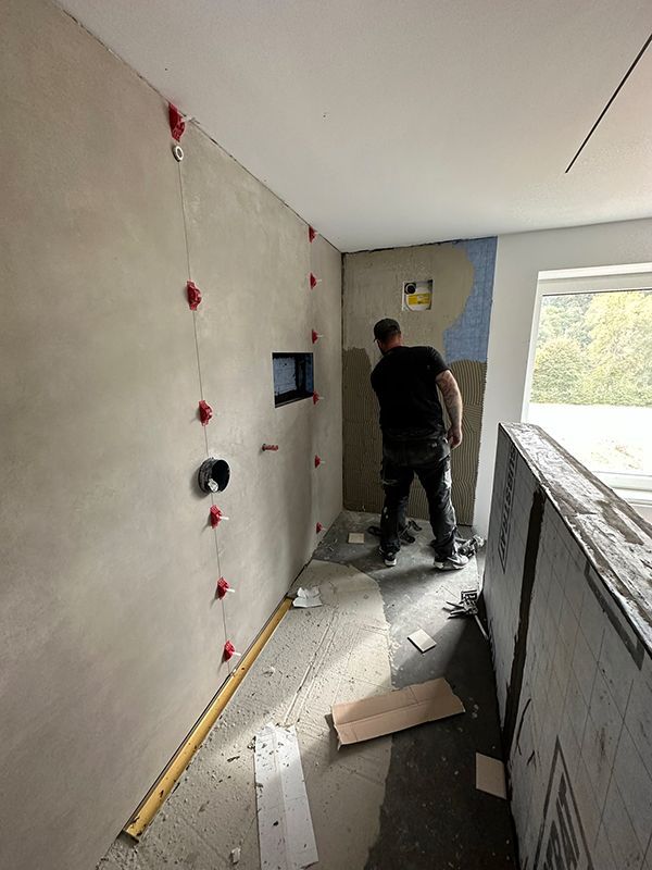 Ein Mann fliest eine Badezimmerwand und setzt Fliesenabstandshalter ein. Bauarbeiten sind im Gange.