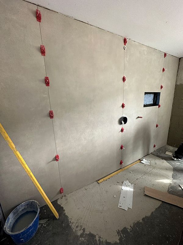 Innenwand im Bau, mit roten Nivellierklammern, Schnur, Rohrleitungen und einem Fensterrahmen.