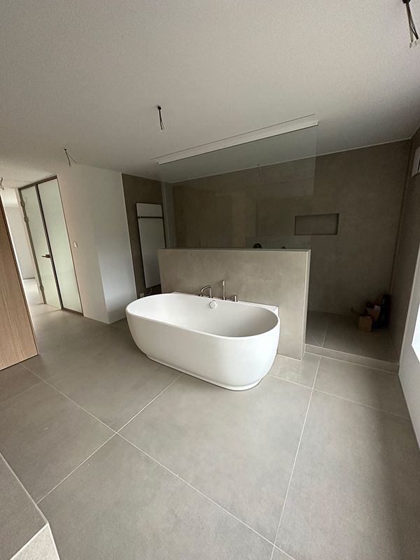 Geräumiges, modernes Badezimmer mit einer freistehenden weißen Badewanne, Fliesen in neutralen Farben und einer Duschkabine aus Glas.