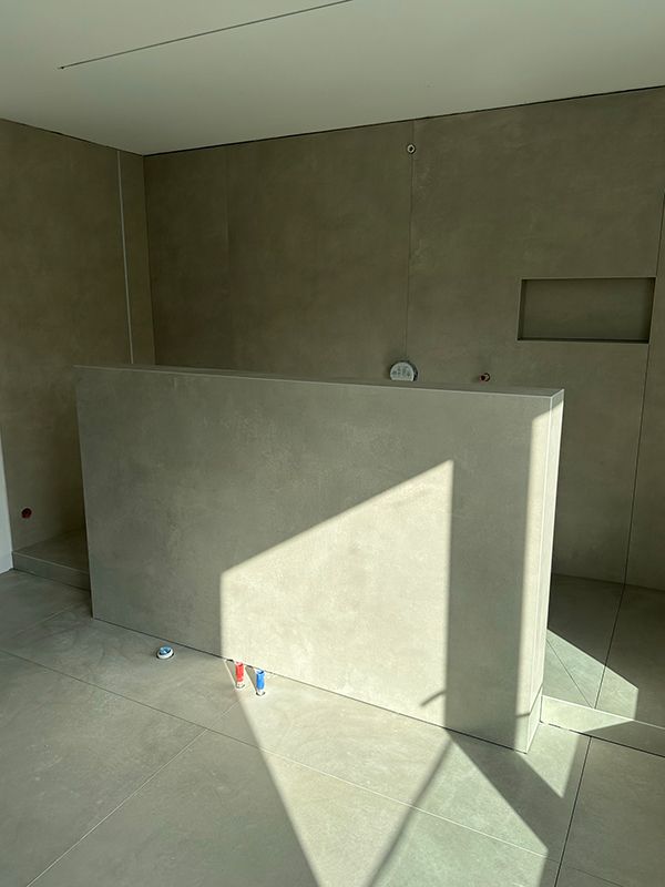 Modernes Badezimmer mit grauen Wänden, Betontrennwand und Fliesenboden. Sonnendurchflutetes Interieur, minimalistisches Design.