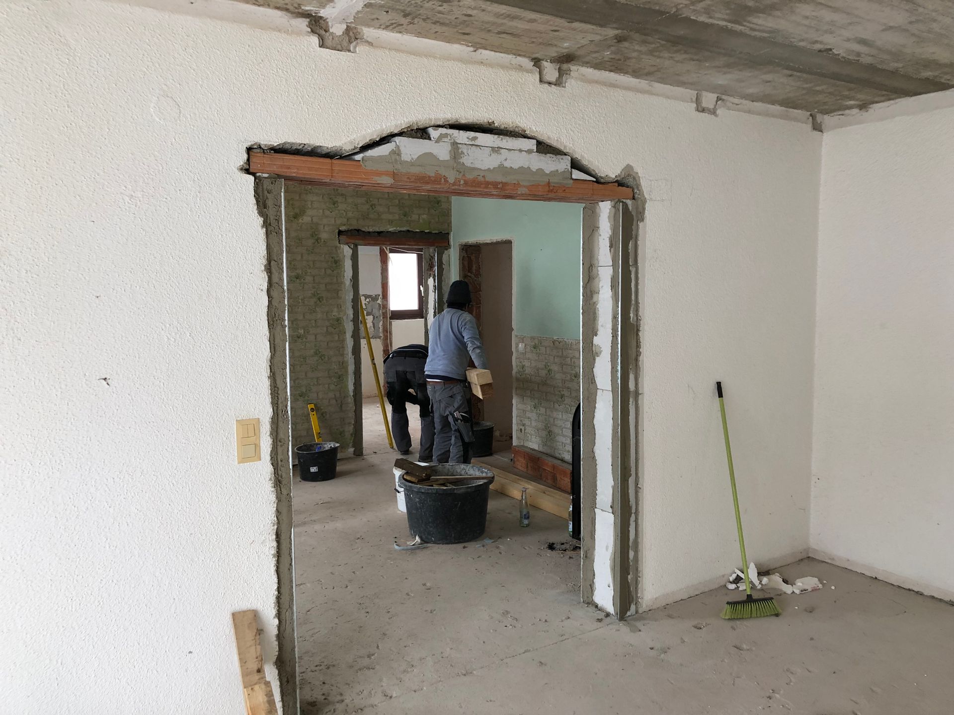 Bau eines gewölbten Torbogens. Zwei Personen arbeiten in einem Raum mit Schutt und Werkzeug.
