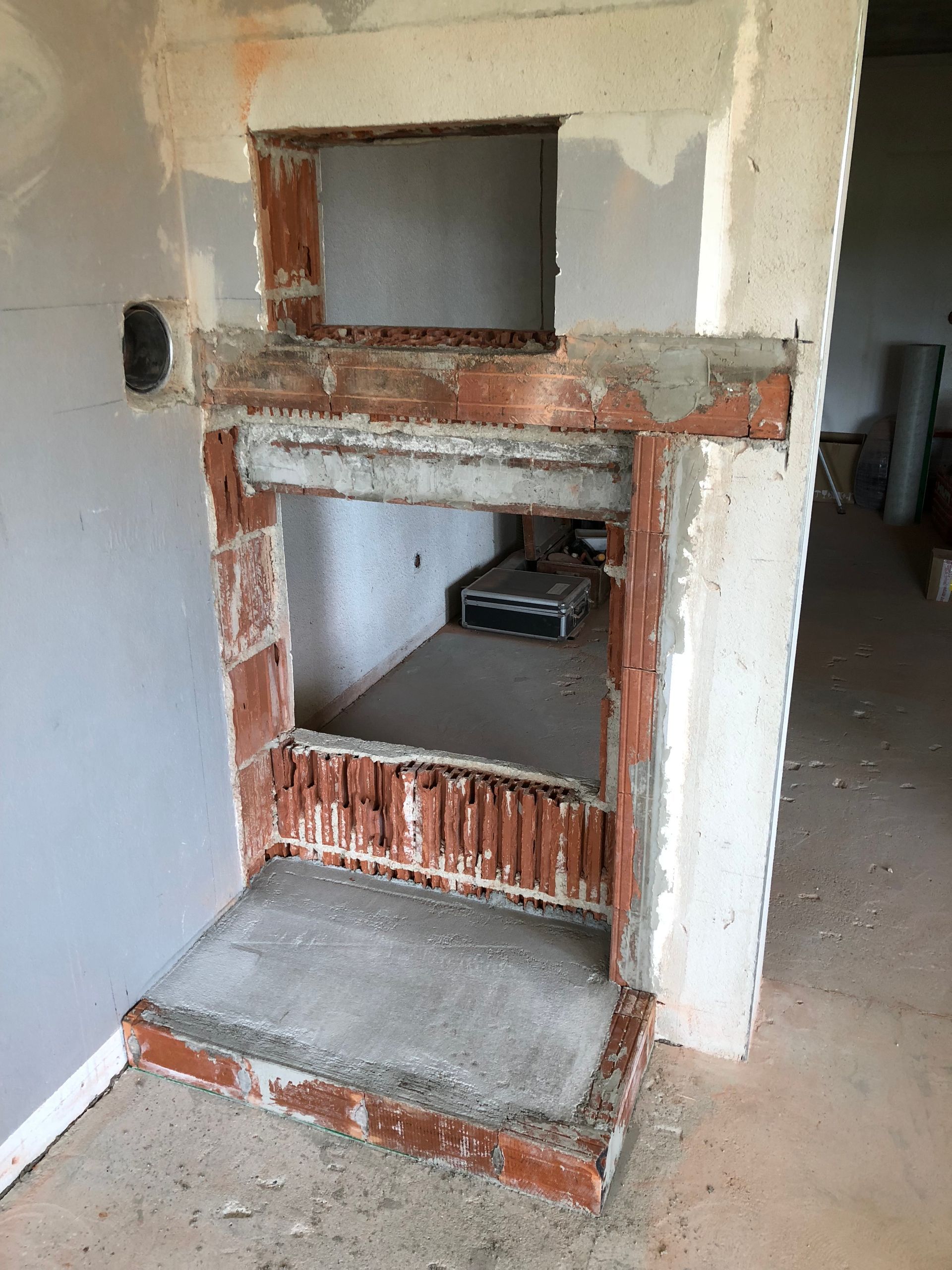 Im Bau befindlicher gemauerter Kamin mit offenem Innenraum, Betonsockel und unfertigen Umfassungswänden.
