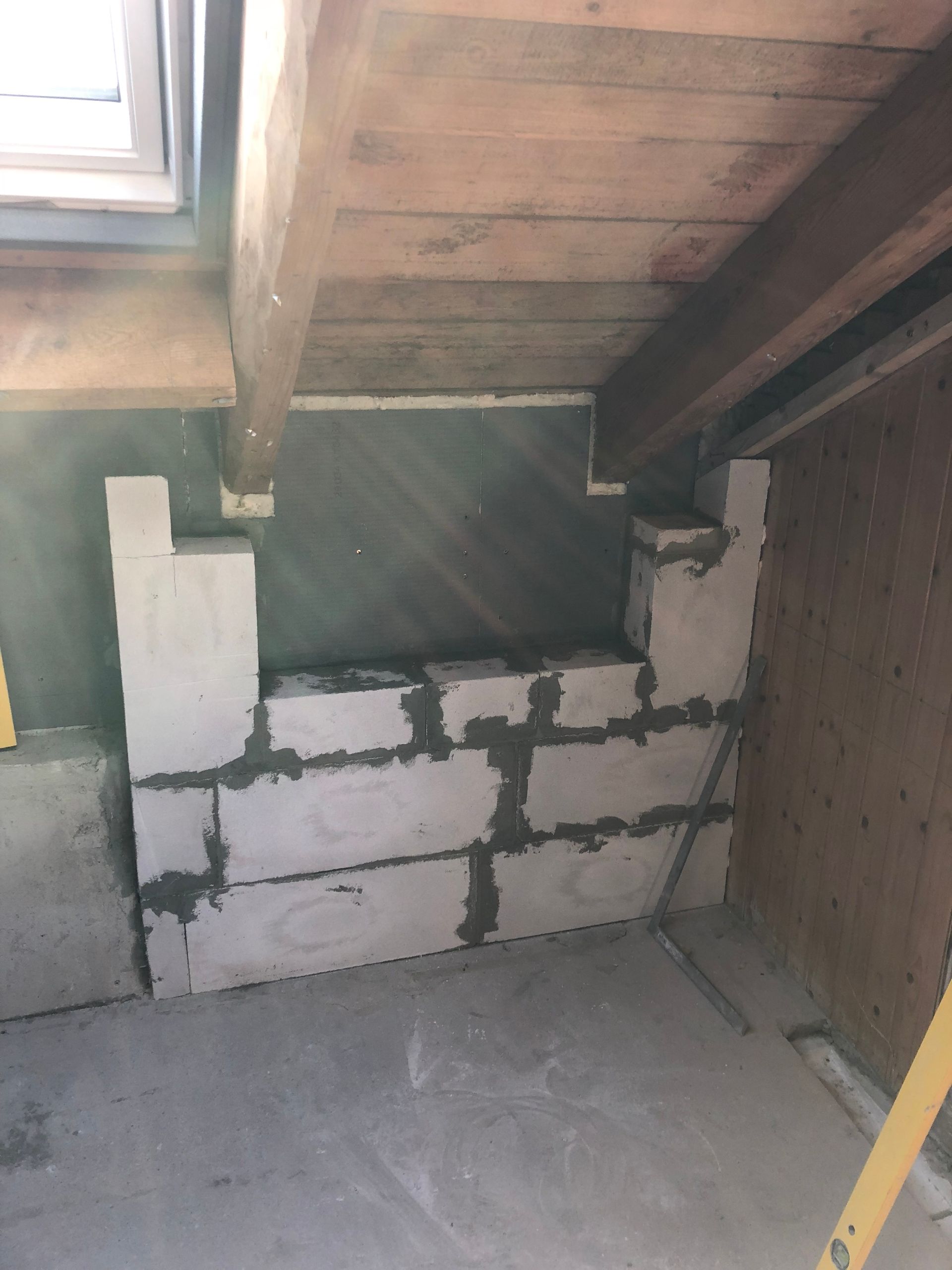 Innenausbau: weiße Blockwand unter Holzbalkendecke, graue Wände und Betonboden.