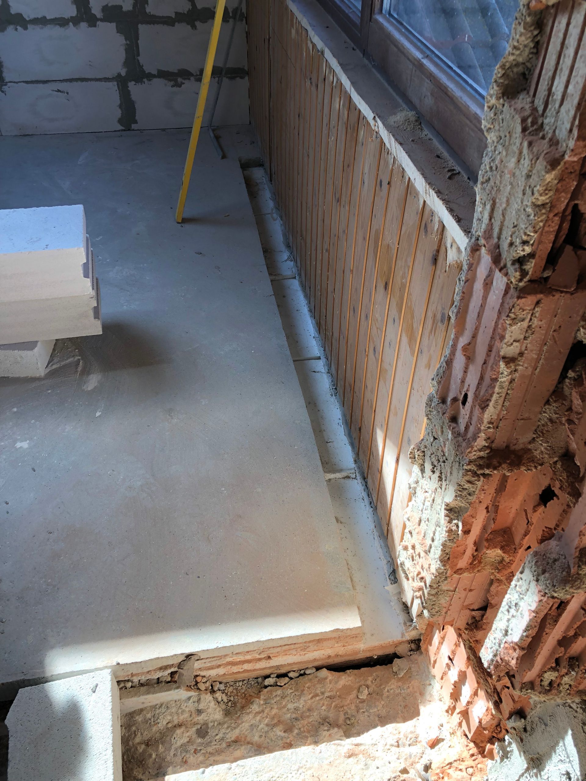 Innenansicht während der Bauphase, Betonboden, Ziegelwand, Fenster, Holzrahmen mit Isolierung und eine Wasserwaage.
