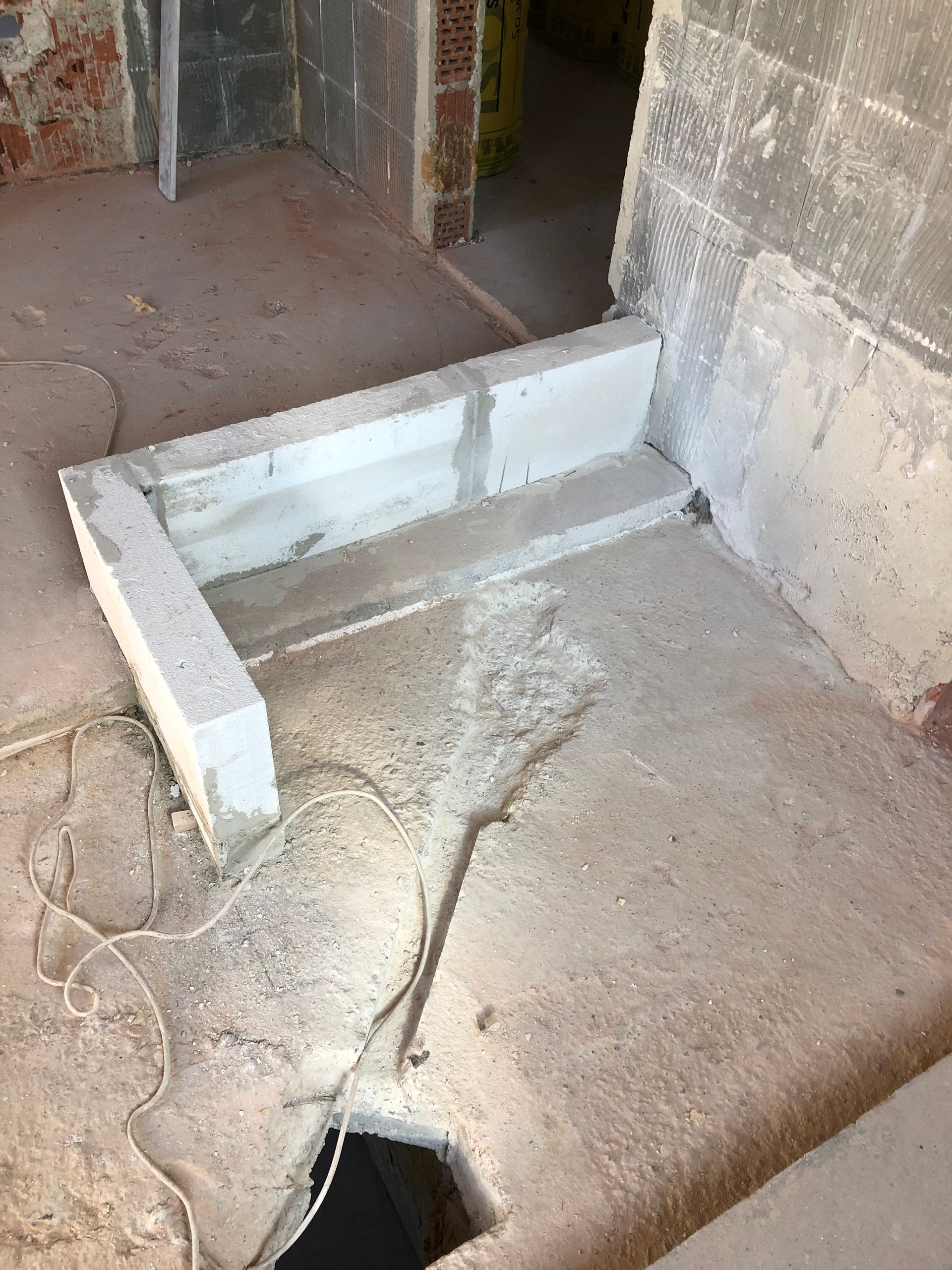 Baustelle: Betonboden mit erhöhter, rechteckiger Blockstruktur. Freiliegende Leitungen.