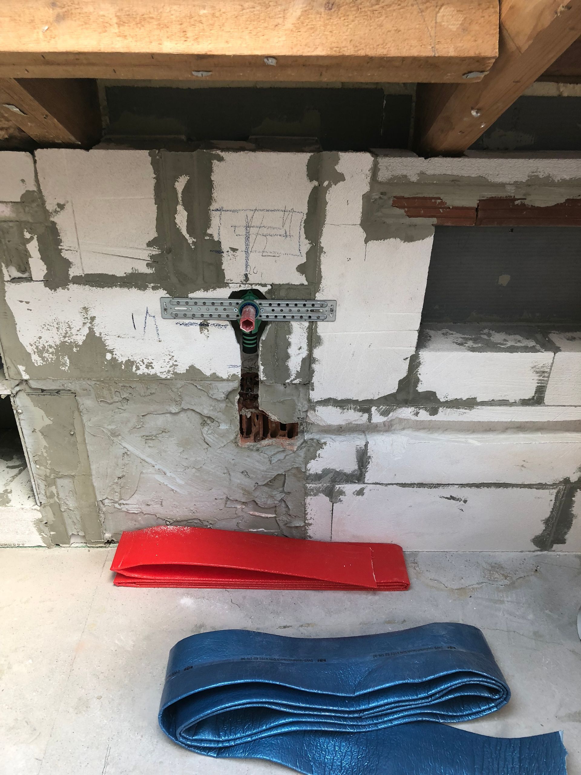 Baustelle: Elektroarbeiten an einer weißen Ziegelwand. Darunter liegen rote und blaue Schutzmaterialien.