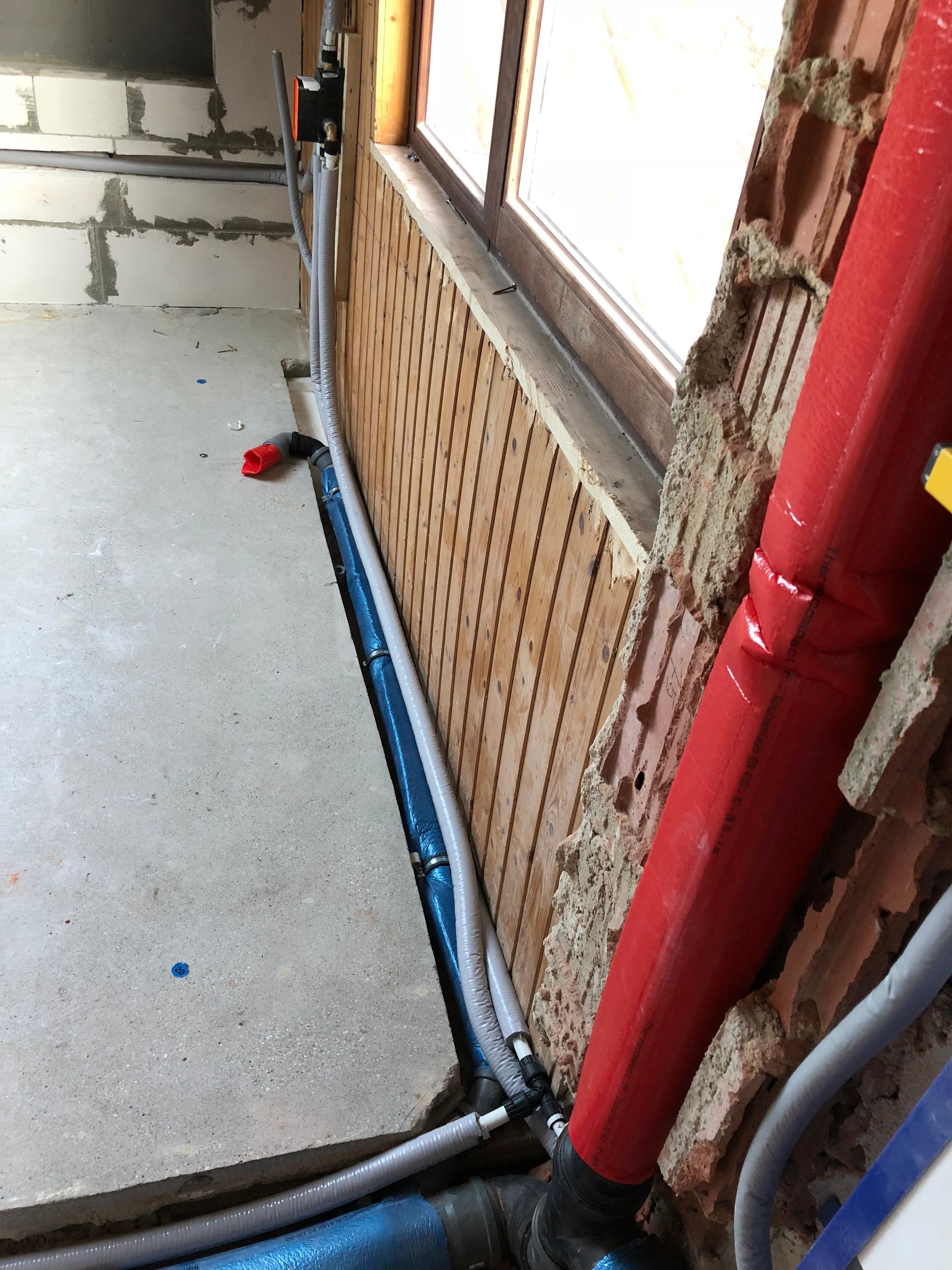Innenansicht der Baustelle: Rohre entlang der Wand, Ziegel, Betonboden.