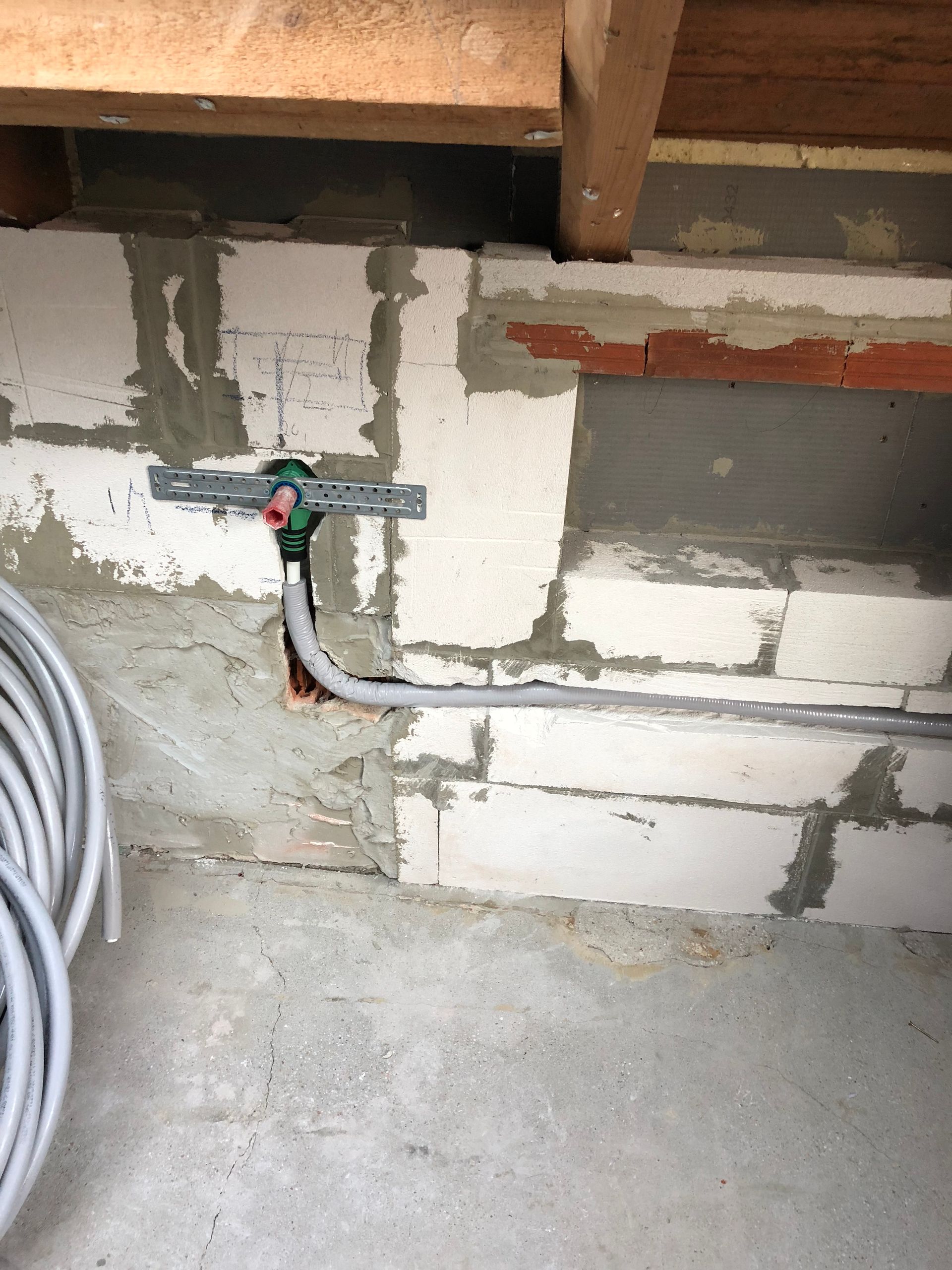 Weiße Blockwand mit Leitungen und Elektrogeräten. Betonboden und Holzbalkendecke sichtbar.