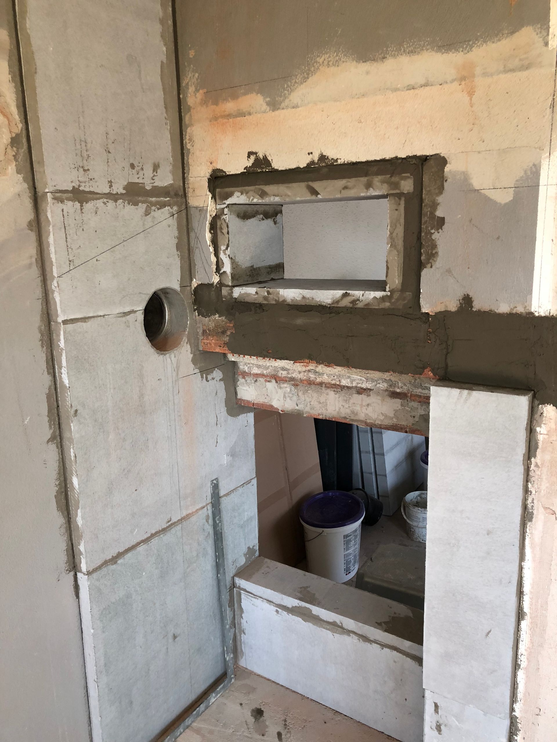 Baustelle: unfertiger Kamin mit rechteckiger Öffnung, grauen Betonwänden und einem runden Rohr.