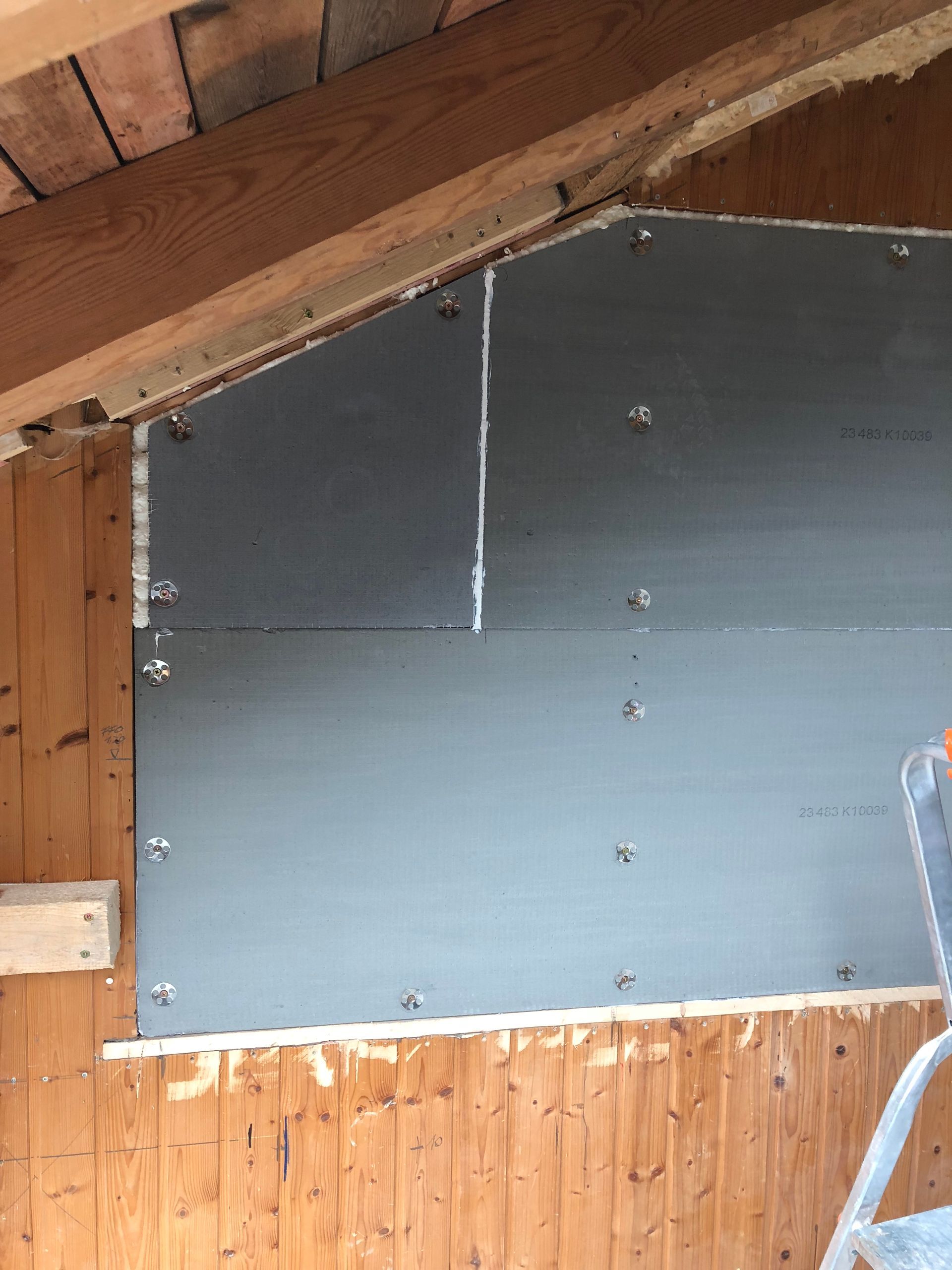 Innenansicht: teilweise auf einer Holzwand angebrachte graue Trockenbauwand, die den Blick auf den Holzrahmen freigibt.