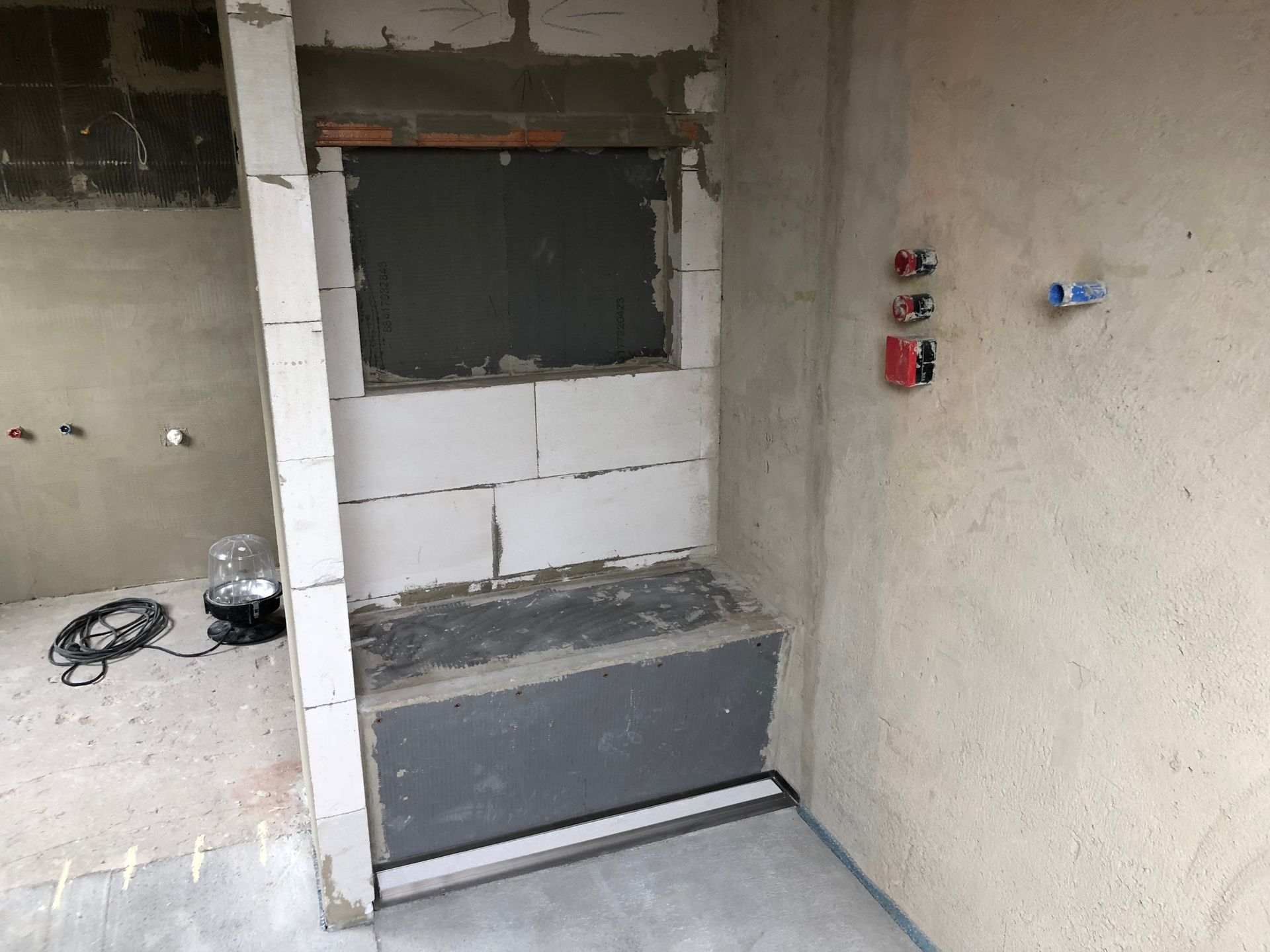 Bau eines Badezimmers. Graue Duschbank mit Abfluss. Sanitärarmaturen an der Wand.