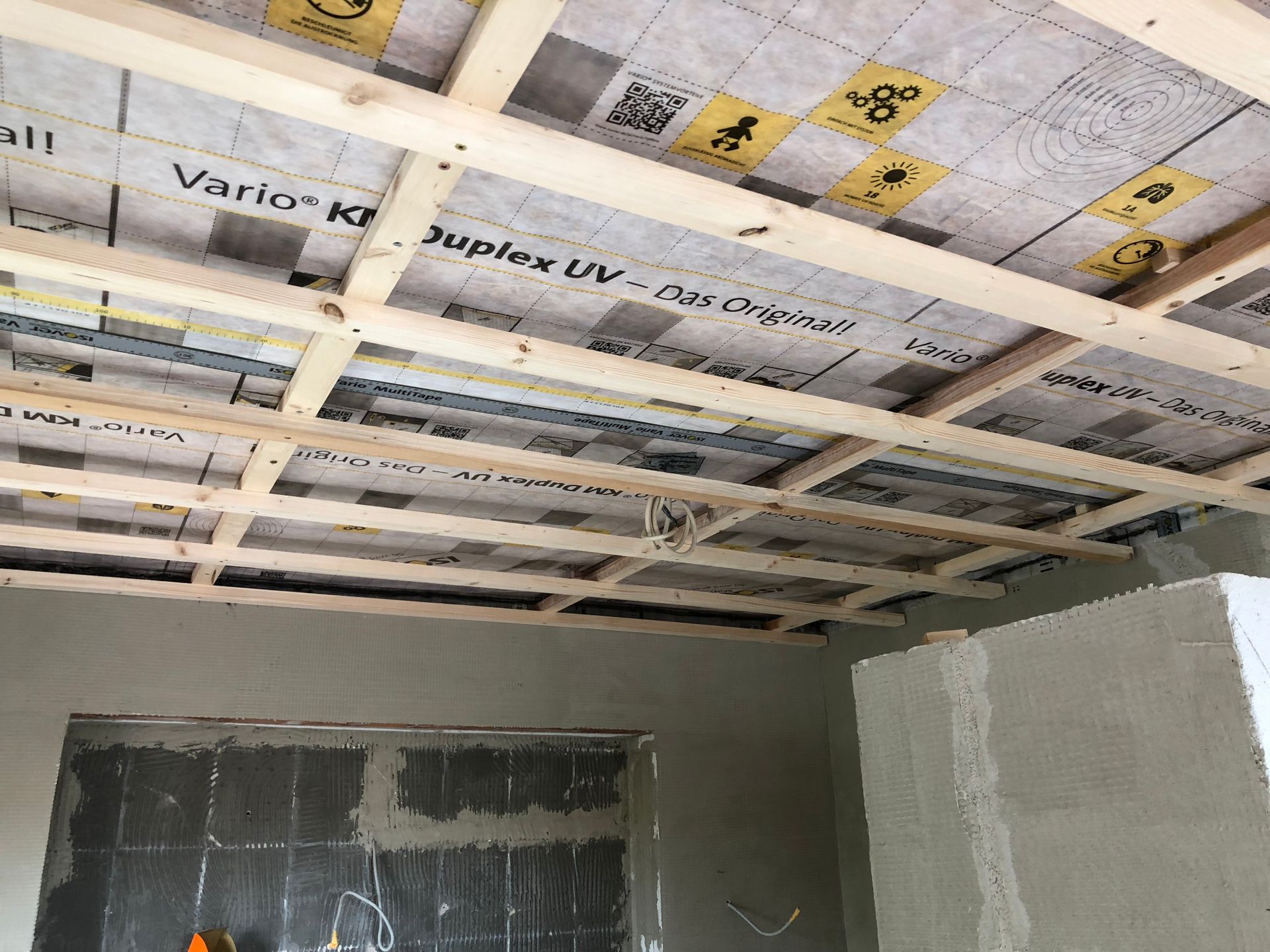 Innenausbau mit Holzdeckenrahmen mit Isolierung und Rohrleitungen, teilweise fertiggestellte Wände.