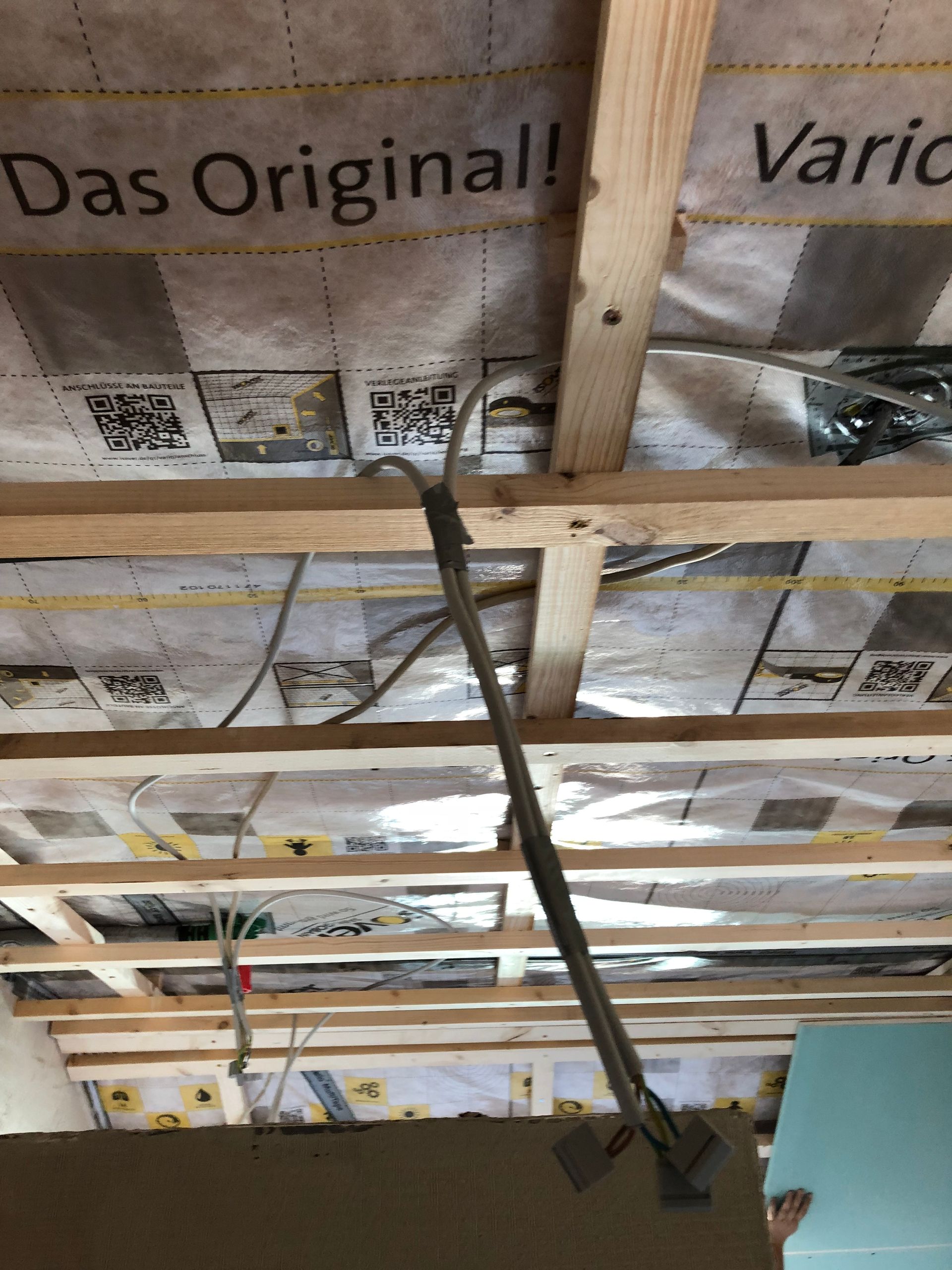 Von den Deckenbalken hängen elektrische Leitungen, Isolierung und Trockenbau sind sichtbar.