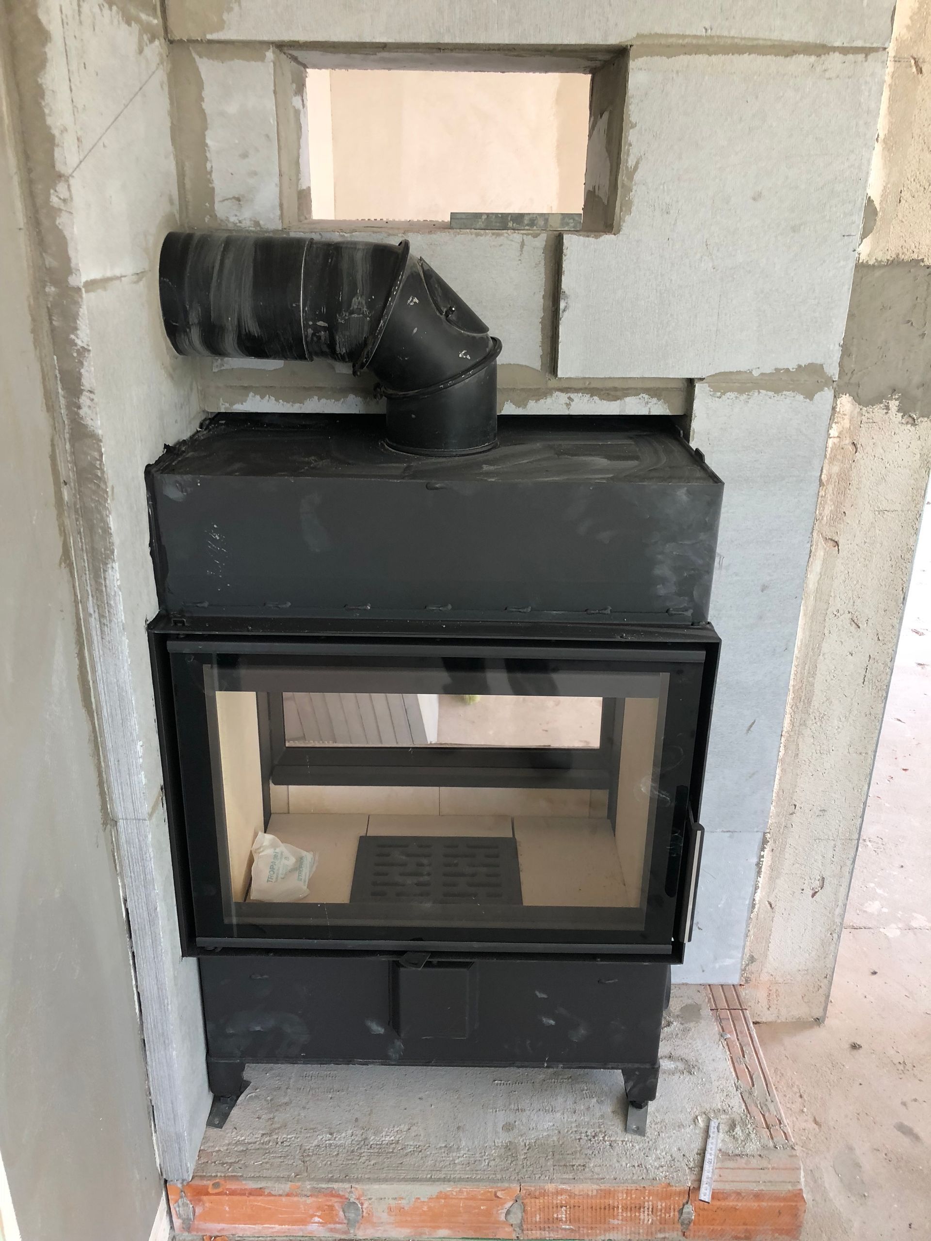 Schwarzer Kamin, eingebaut in eine teilweise errichtete graue Ziegelwand, mit schwarzem Rauchabzug und offener Oberseite.
