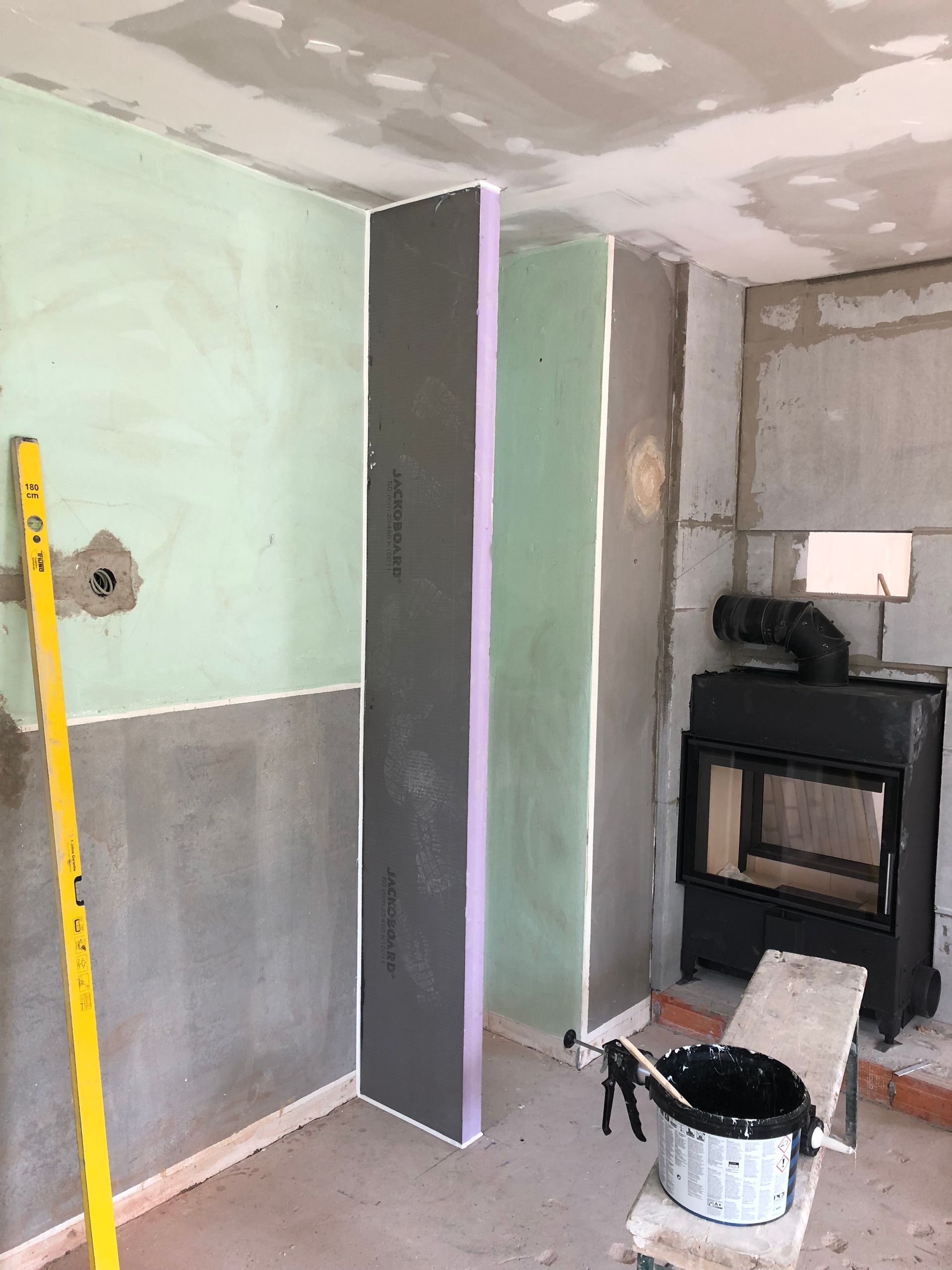 Baustelle mit Kamin, Wände aus grauer, grüner und grau-violetter Isolierung. Nivellierwerkzeug in der Ecke.