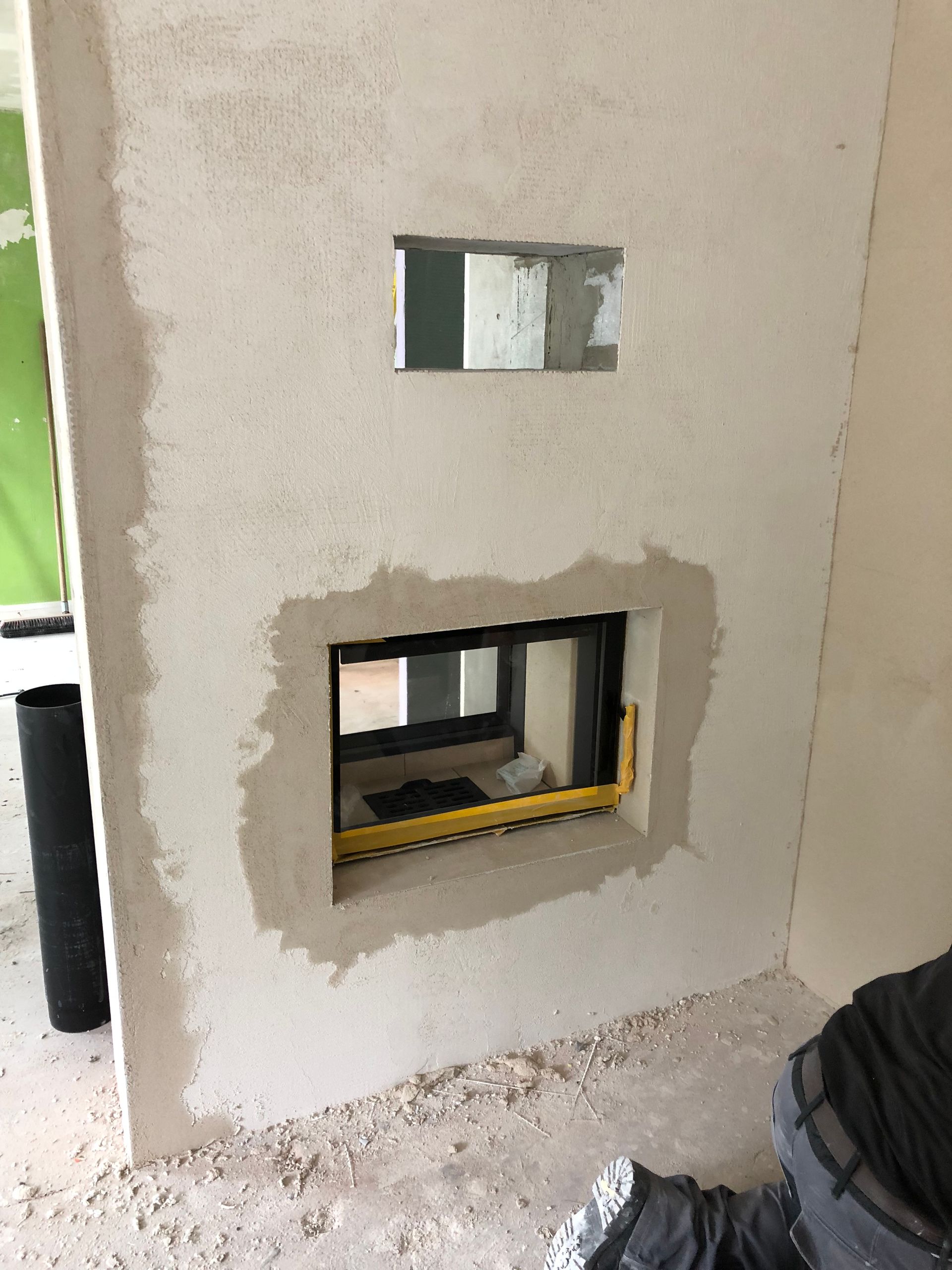 Baustelle mit Wand, die rechteckige Öffnungen für ein Fenster aufweist. Putz und eine Wasserwaage sind sichtbar.