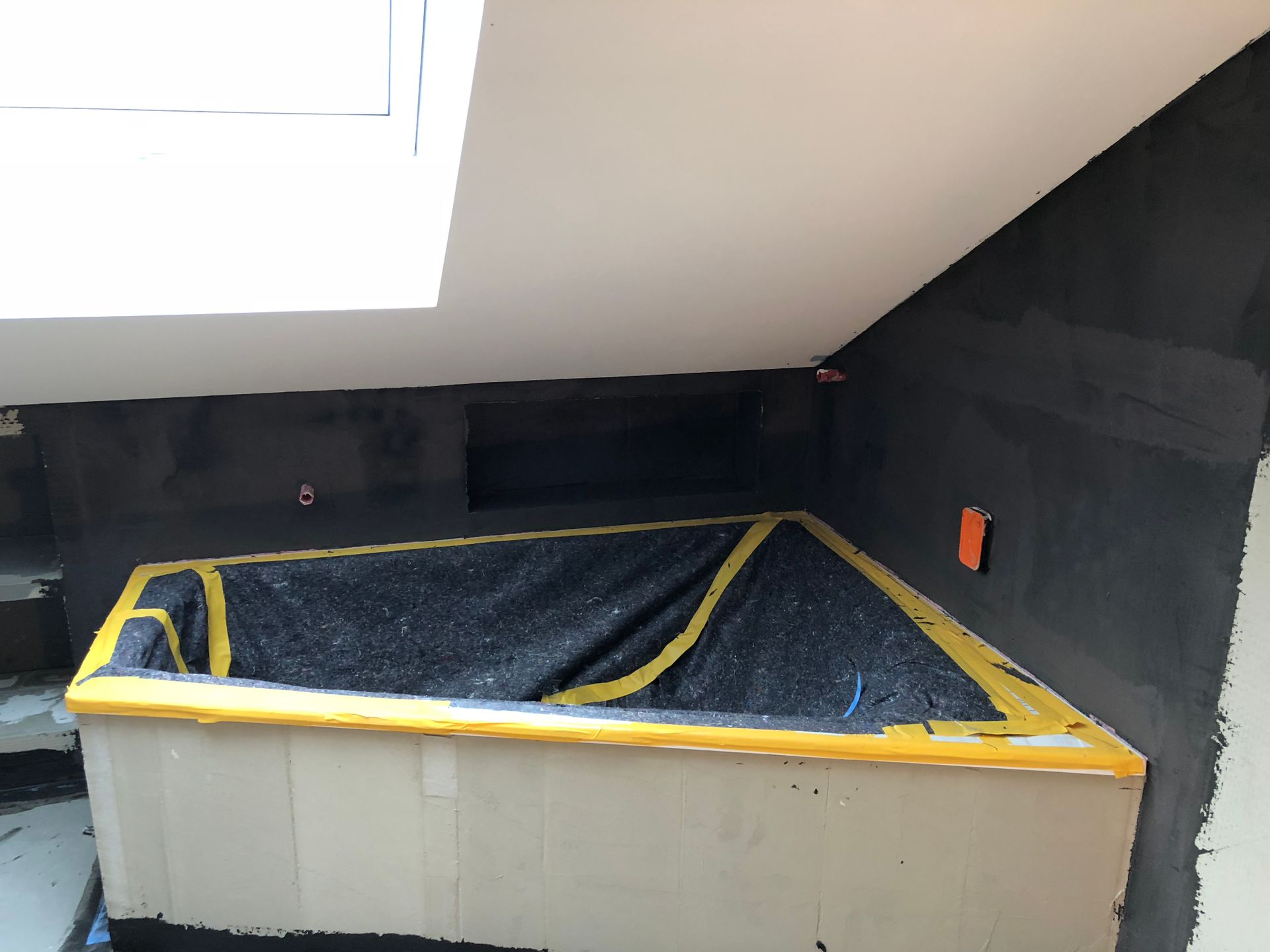 Im Bau befindliches Badezimmer mit eingebauter Badewanne, dunklen Wänden und Oberlicht.