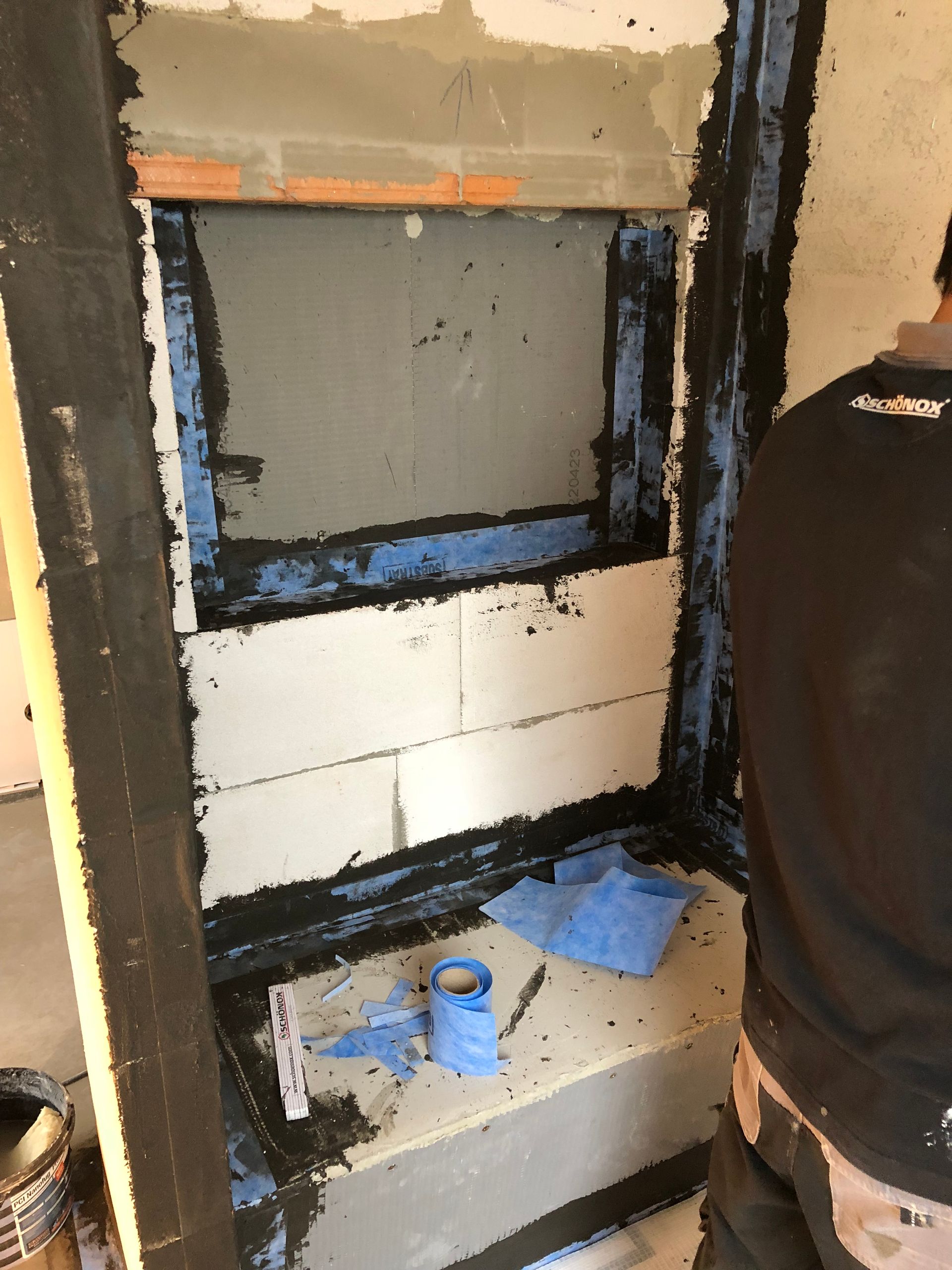 Baustelle mit einer Nische, Abdichtungsarbeiten im Gange, ein Mann arbeitet, blaues Klebeband und grauer Mörtel.