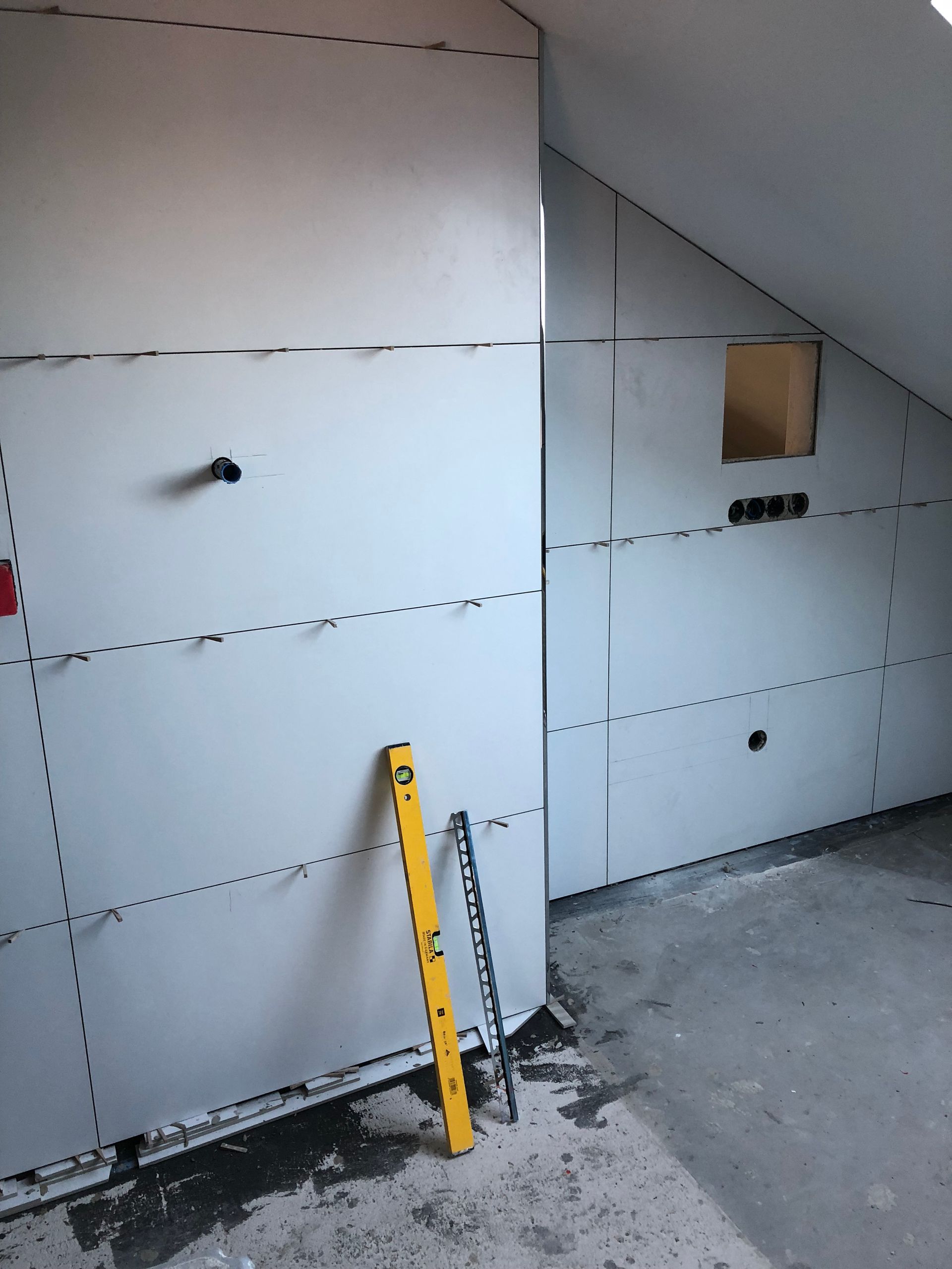 Innenraum im Rohbau, Trockenbauwände, eine Wasserwaage lehnt an der Wand, Steckdosen und unfertiger Boden.