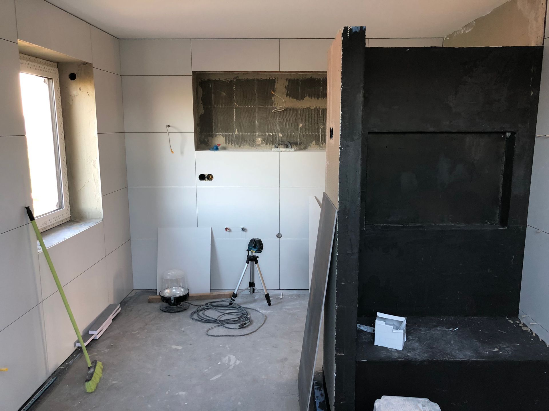 Badezimmer im Bau: Trockenbau installiert, unfertiges Fenster, dunkelgraue Struktur.