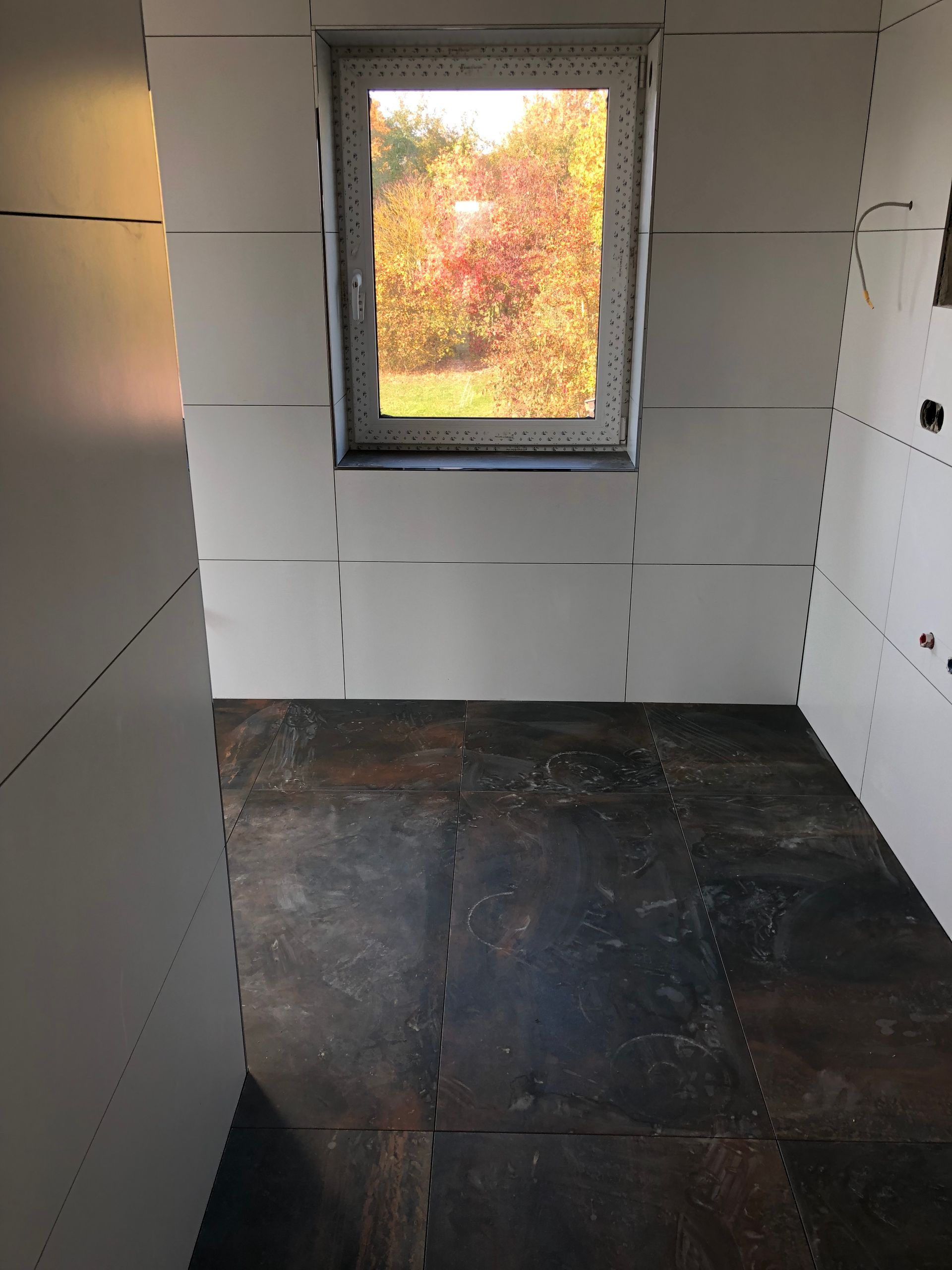 Innenraum mit weißen Wänden, dunklem Boden und einem Fenster mit Blick auf das Herbstlaub.