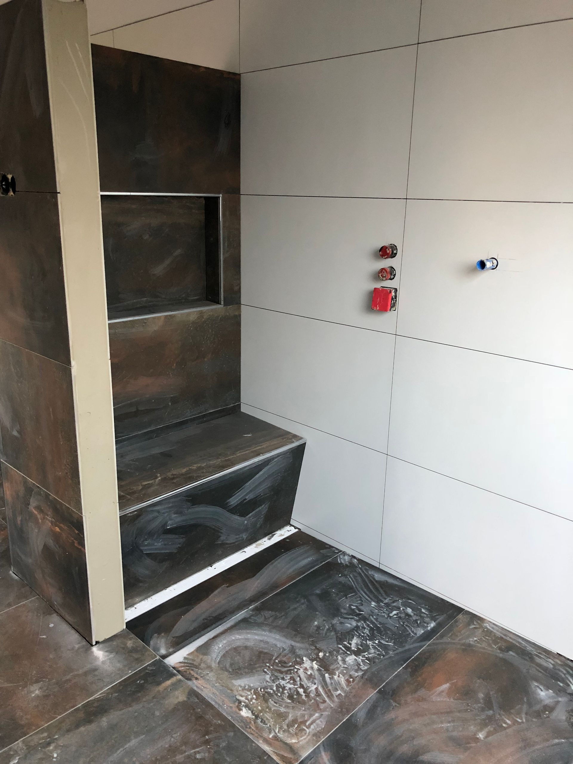Dusche im Bau: dunkle Fliesen, eingebaute Bank und weiße Trockenbauwände.