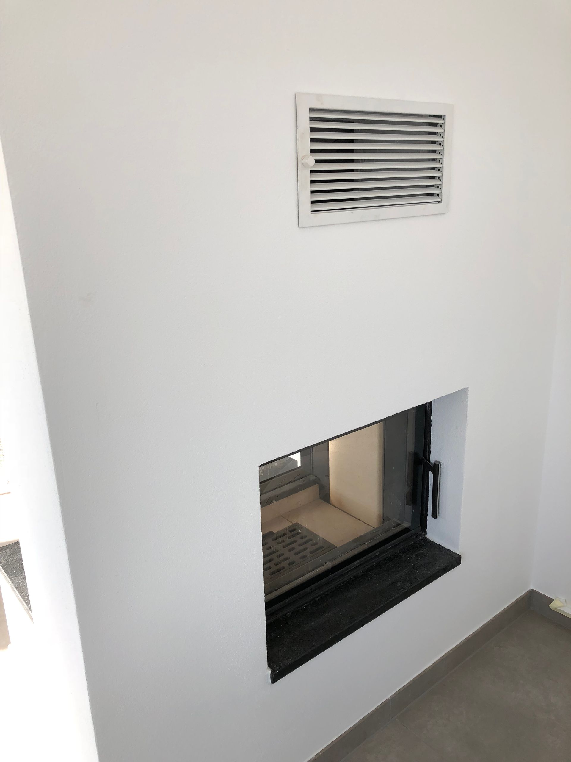 Weiße Wand mit Kamin und Abzug. Der Kamin hat einen schwarzen Rahmen. Darüber befindet sich ein Abzug.