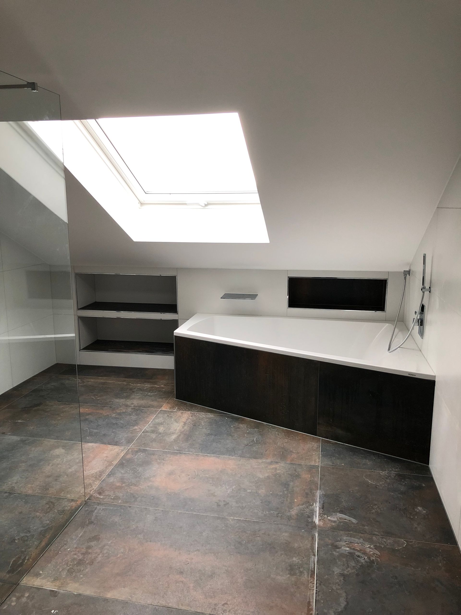 Badezimmer mit Oberlicht, Regalen, Badewannenverkleidung aus dunklem Holz und grauem Bodenbelag.