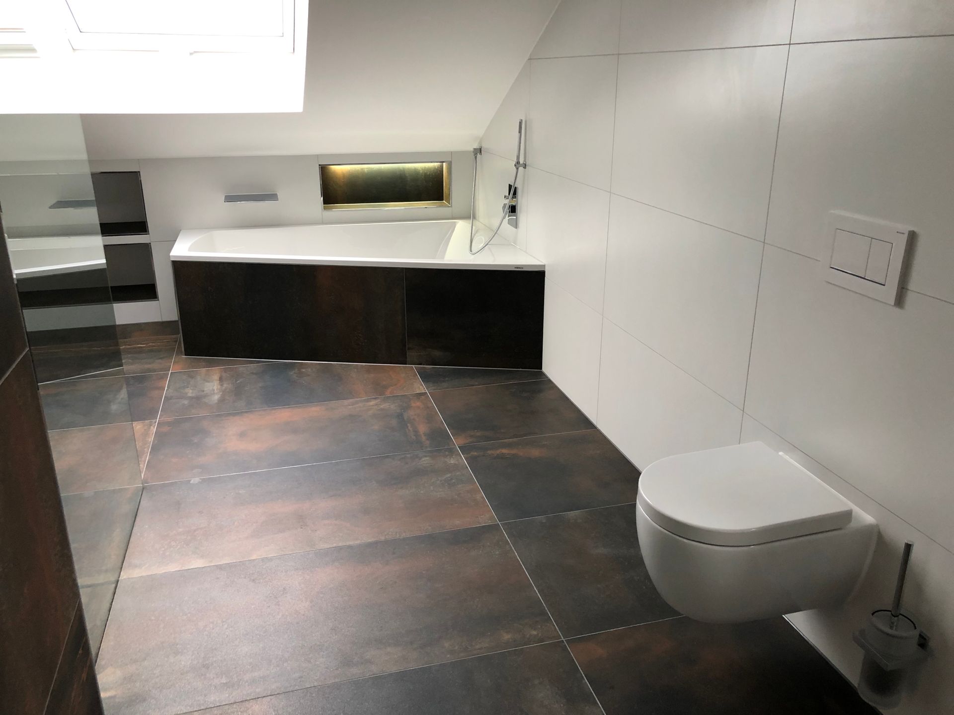 Modernes Badezimmer mit weißen Wänden, Toilette, Badewanne und dunklen, rostfarbenen Bodenfliesen.