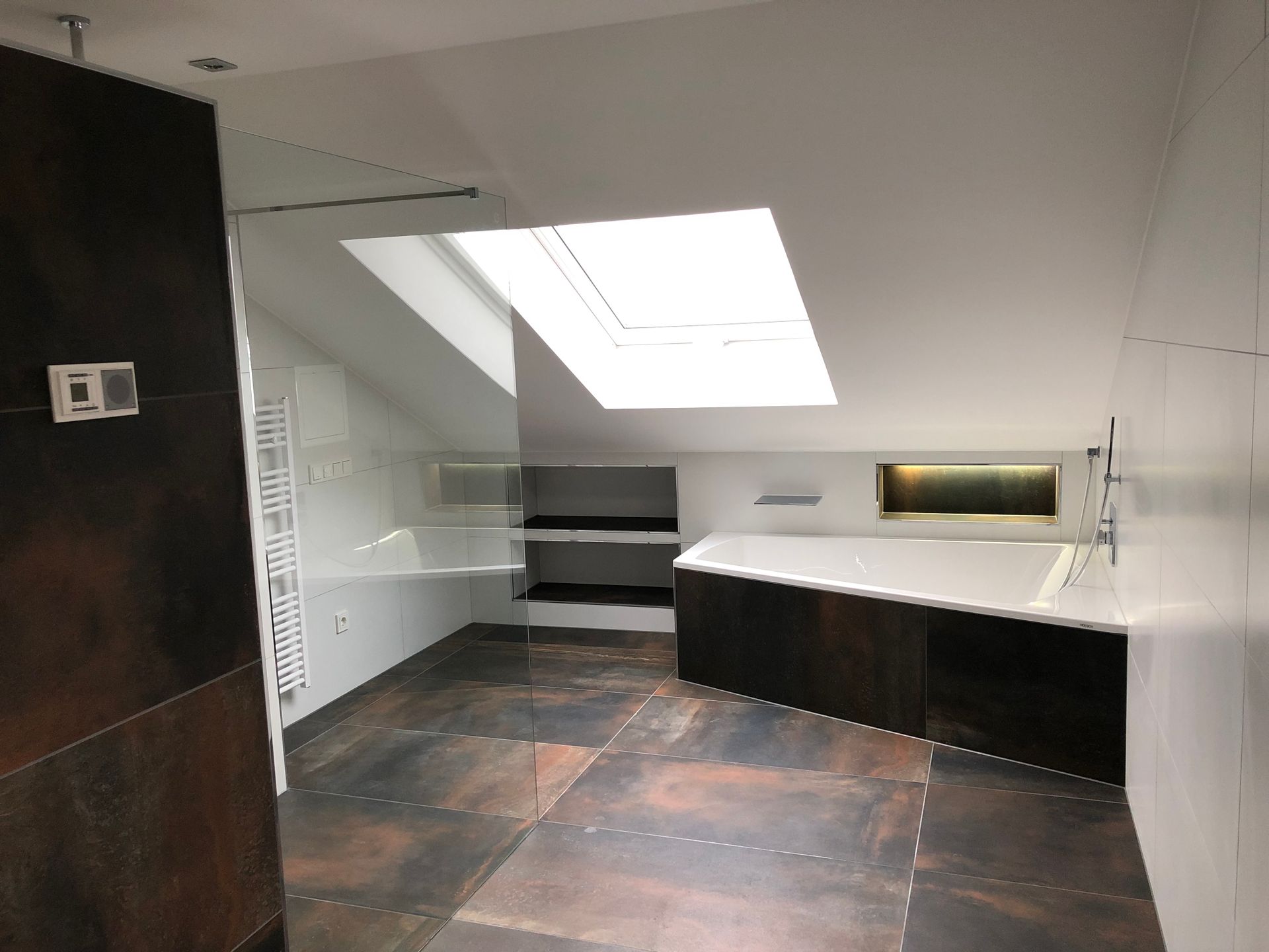 Badezimmer mit Oberlicht, Badewanne und Dusche. Dunkelbraune Fliesen und Akzente sorgen für einen modernen Look.