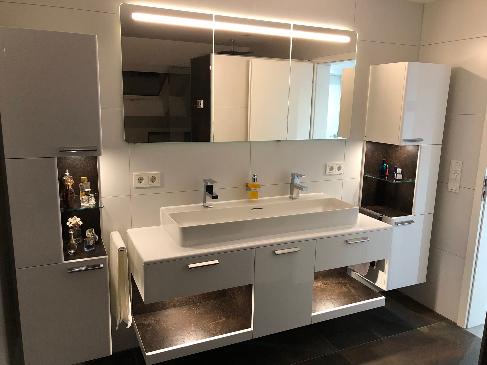 Modernes weißes Badezimmer mit schwebendem Waschtisch, großem Spiegel und Aufbewahrungsschränken.