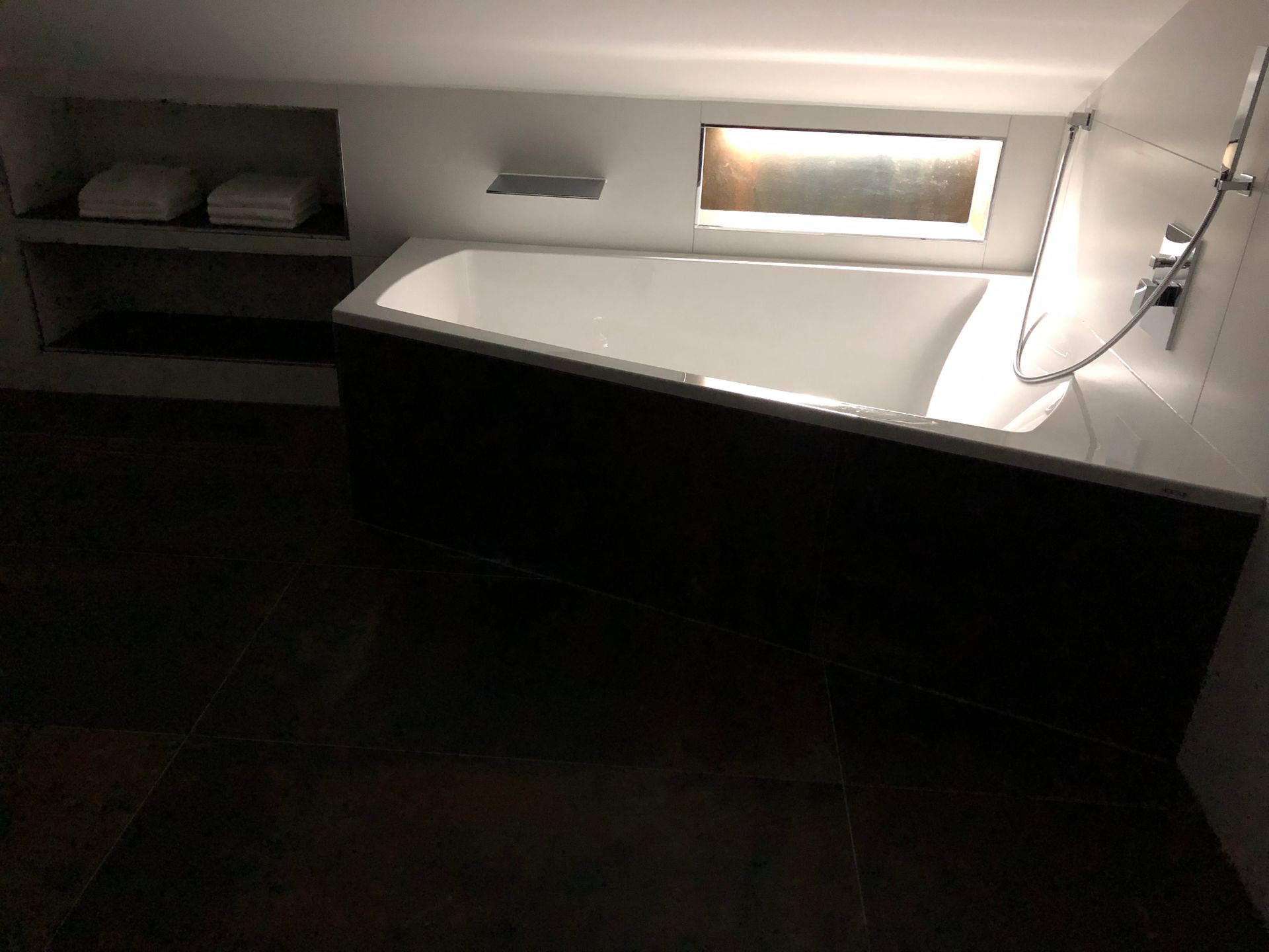 Badezimmer mit Badewanne, Regal mit Handtüchern und dunklem Holzboden.