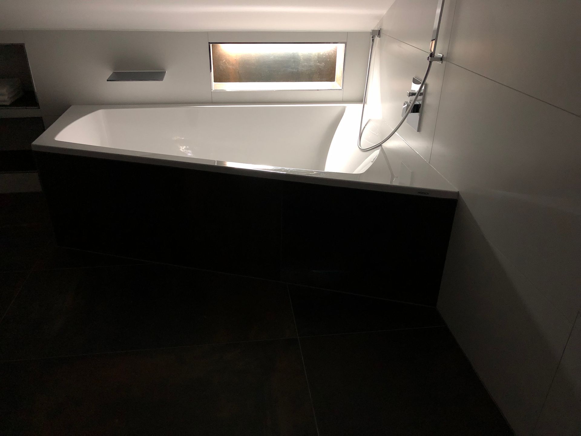 Badewanne in einem modernen Badezimmer mit dunkler Verkleidung und rechteckiger Leuchte.
