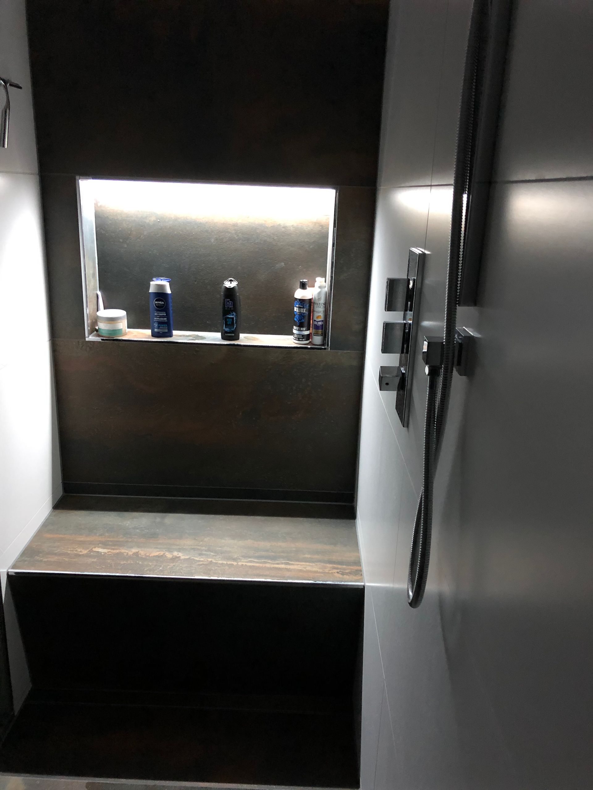 Dusche mit eingebauter Bank und Ablage für Toilettenartikel. Neutrale Farben mit Beleuchtung, silberne Armaturen.
