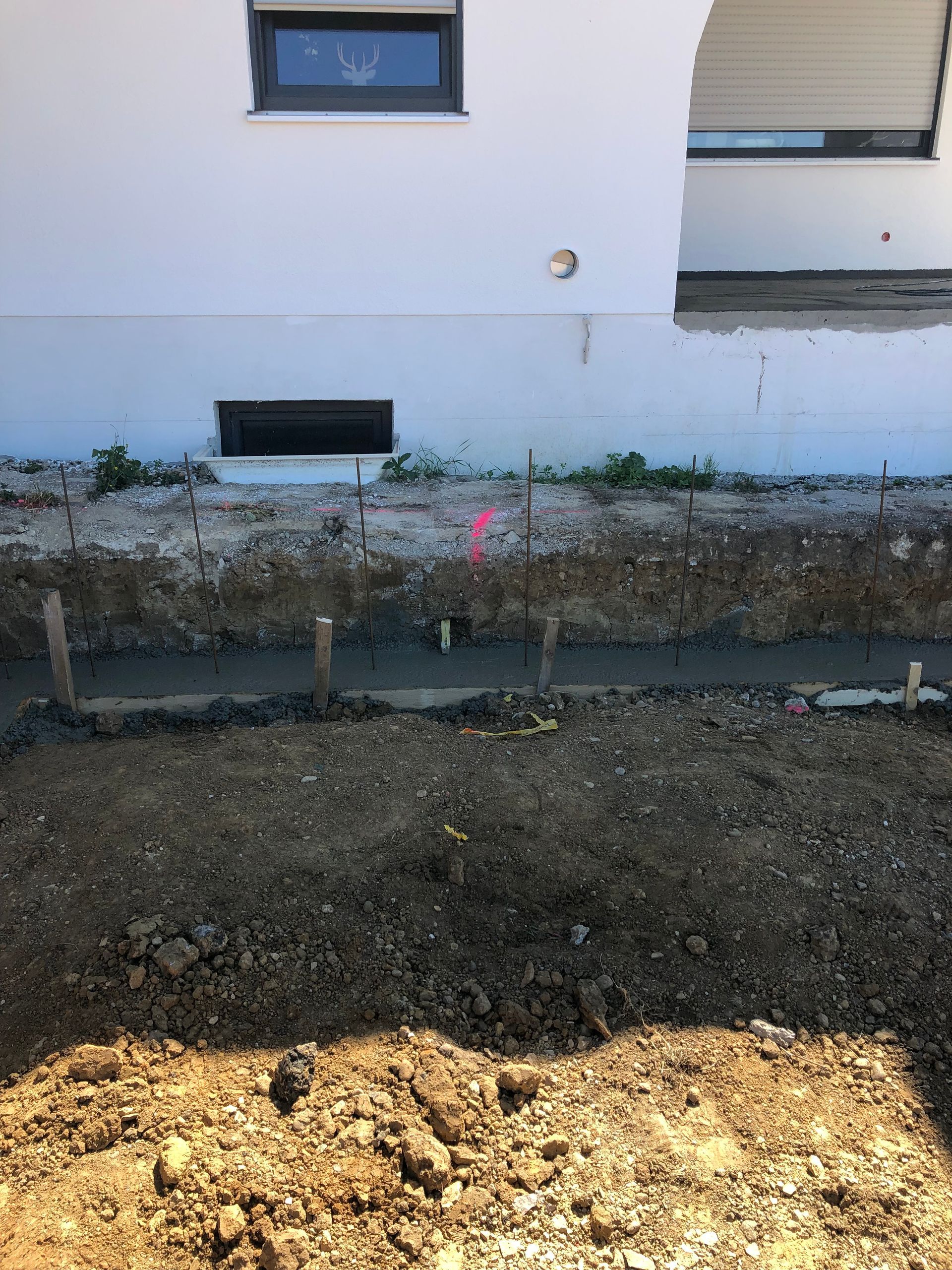 Ein Fundamentgraben in der Nähe eines weißen Gebäudes; Holzpfähle, braune Erde.