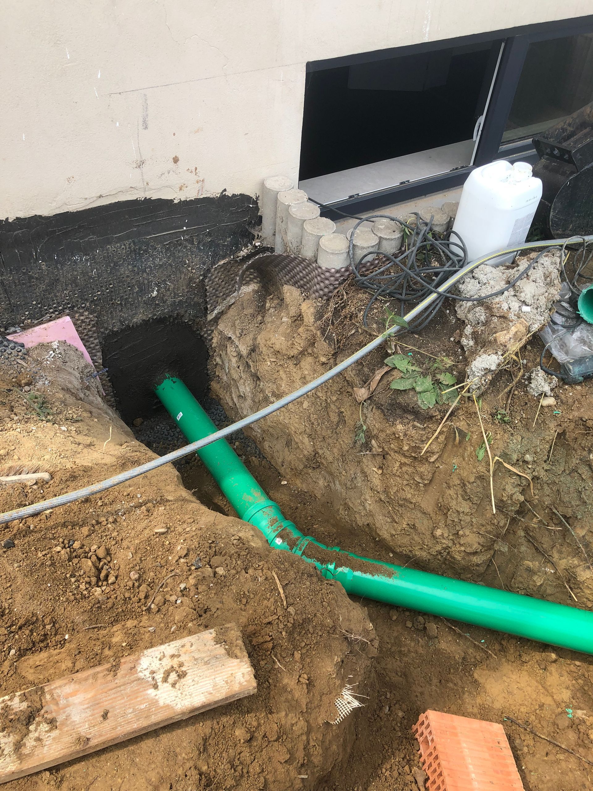 Grünes Rohr, das aus einem Loch im Boden in der Nähe eines Gebäudes ragt, mit einem sichtbaren Fenster.